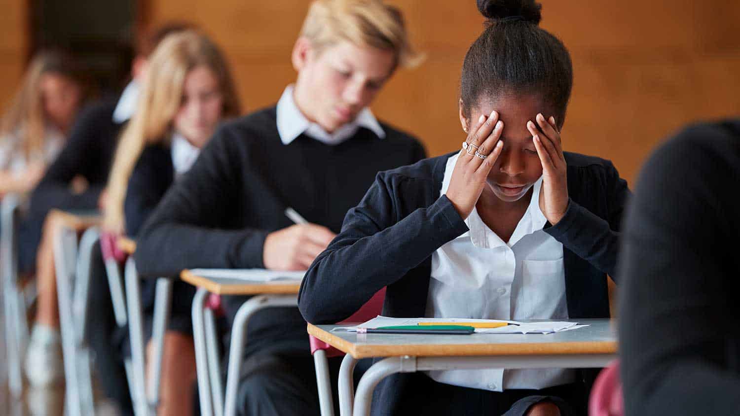 Teenagers taking an exam, one holds her head in her hands