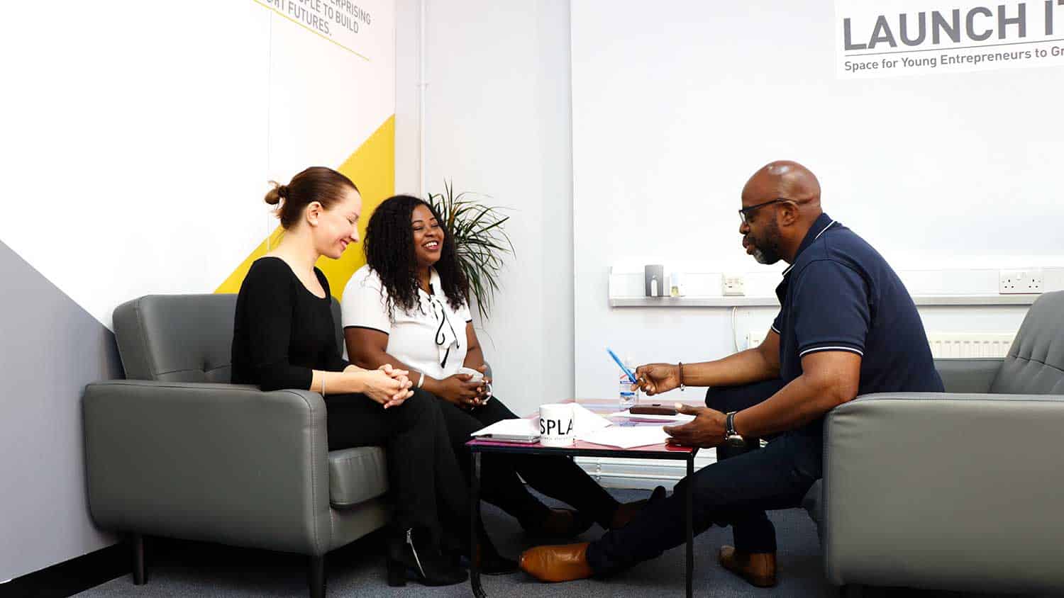 A group of three people discussing something around a desk, looking cheerful