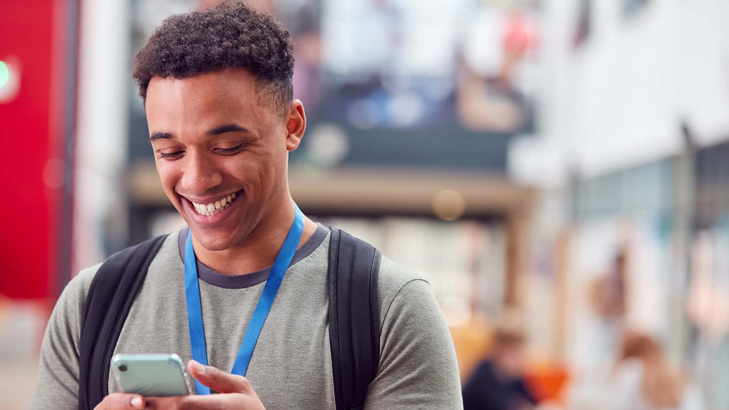 Smiling male college student checking mobile phone in busy communal campus building