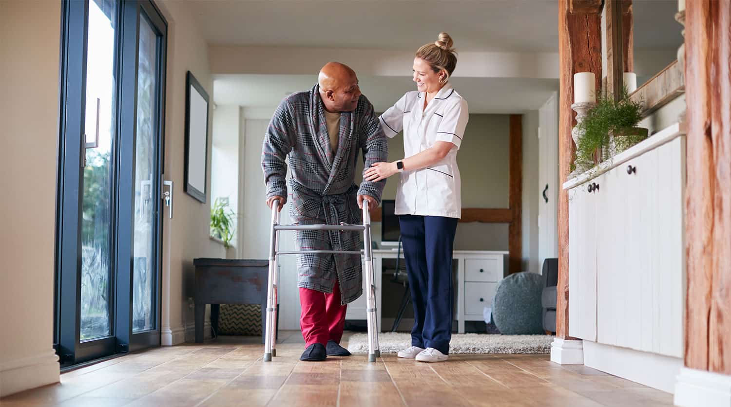 A man using a walker getting assistance from a carer