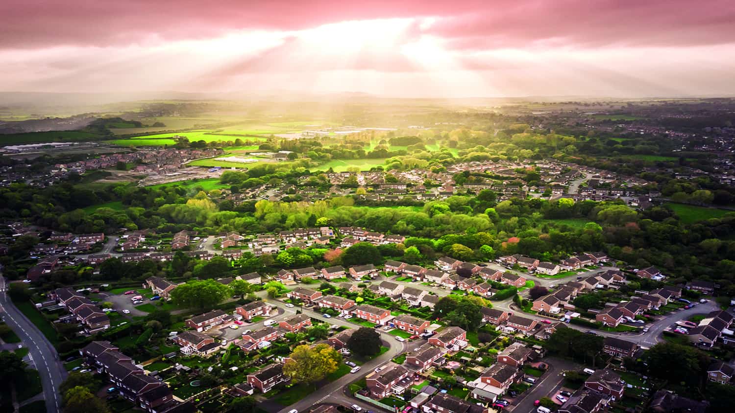 Sun bursting through clouds over traditional British houses with countryside in the background.