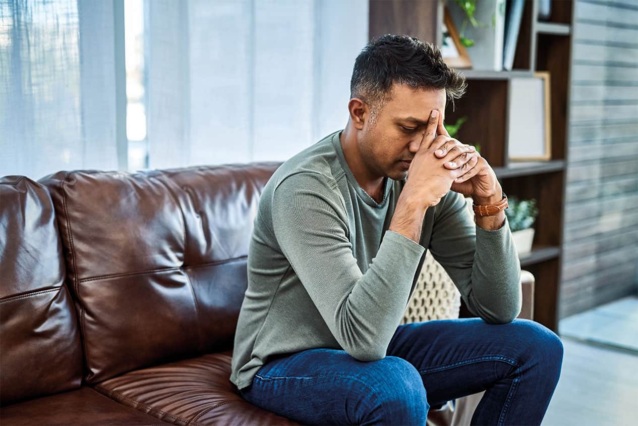 Man sat on a sofa with his head in his hands looking stressed