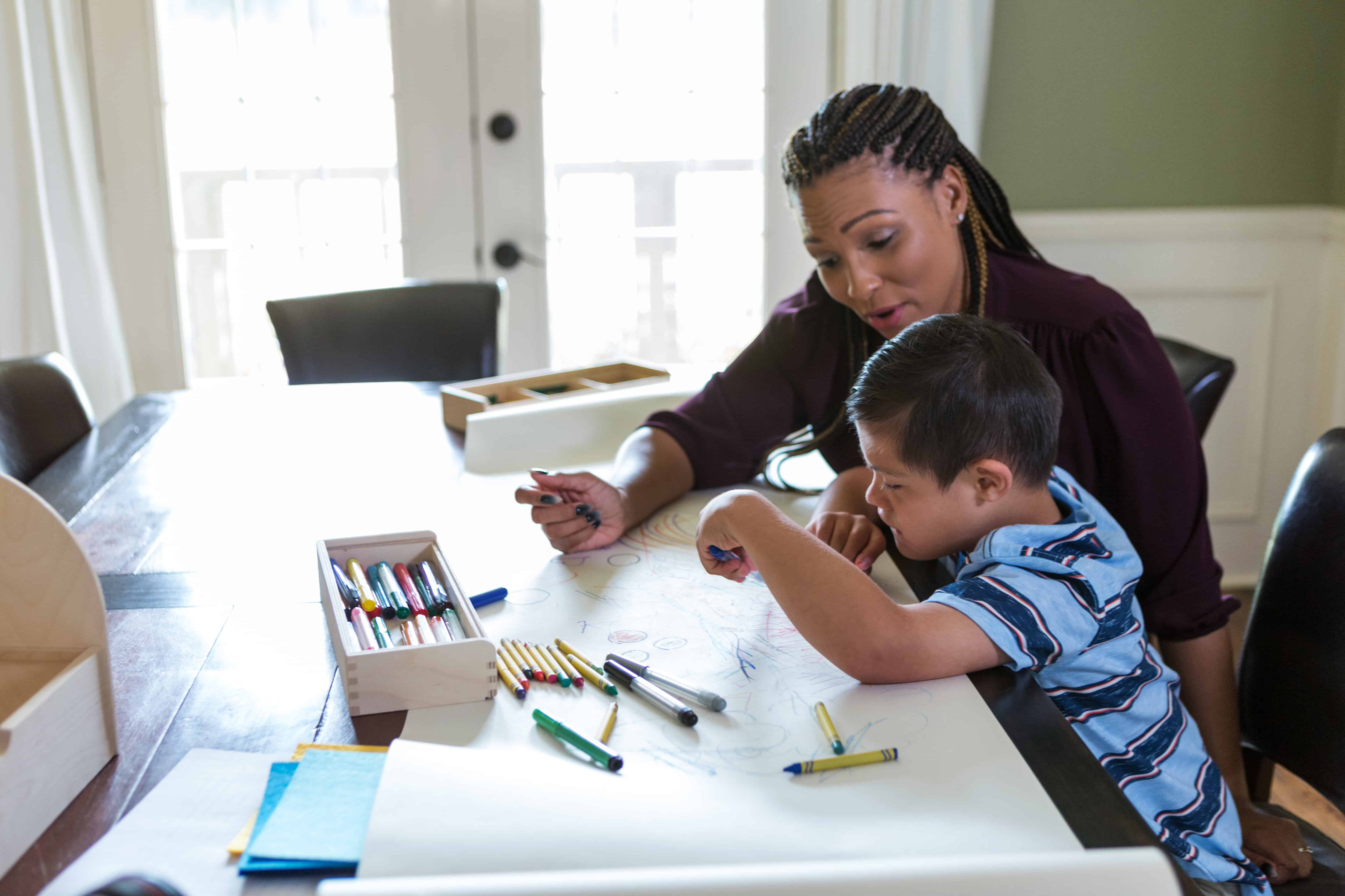 Adult therapist sitting at a table doing drawings with a young child