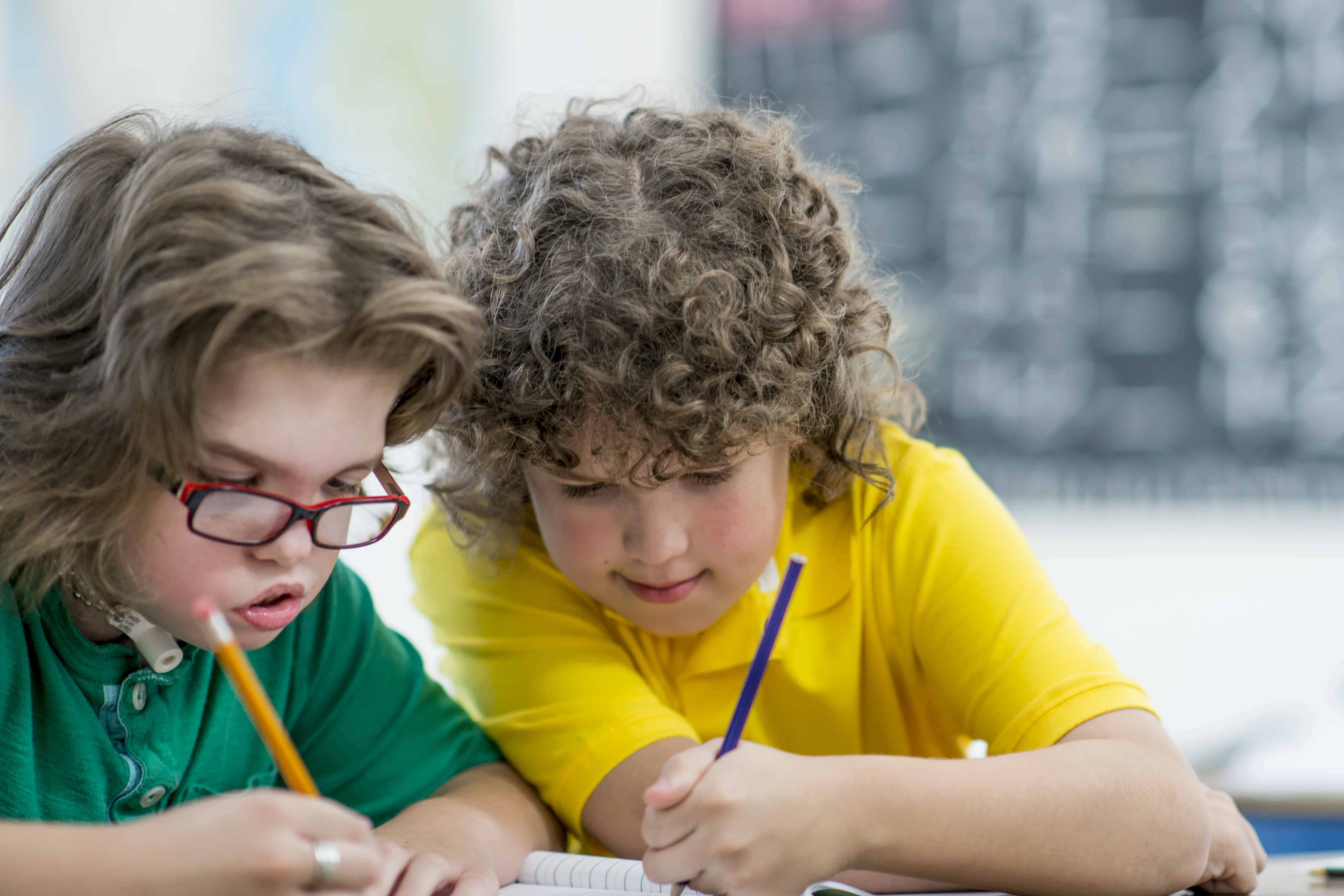 Two primary school aged boys writing in a notebook together in class.