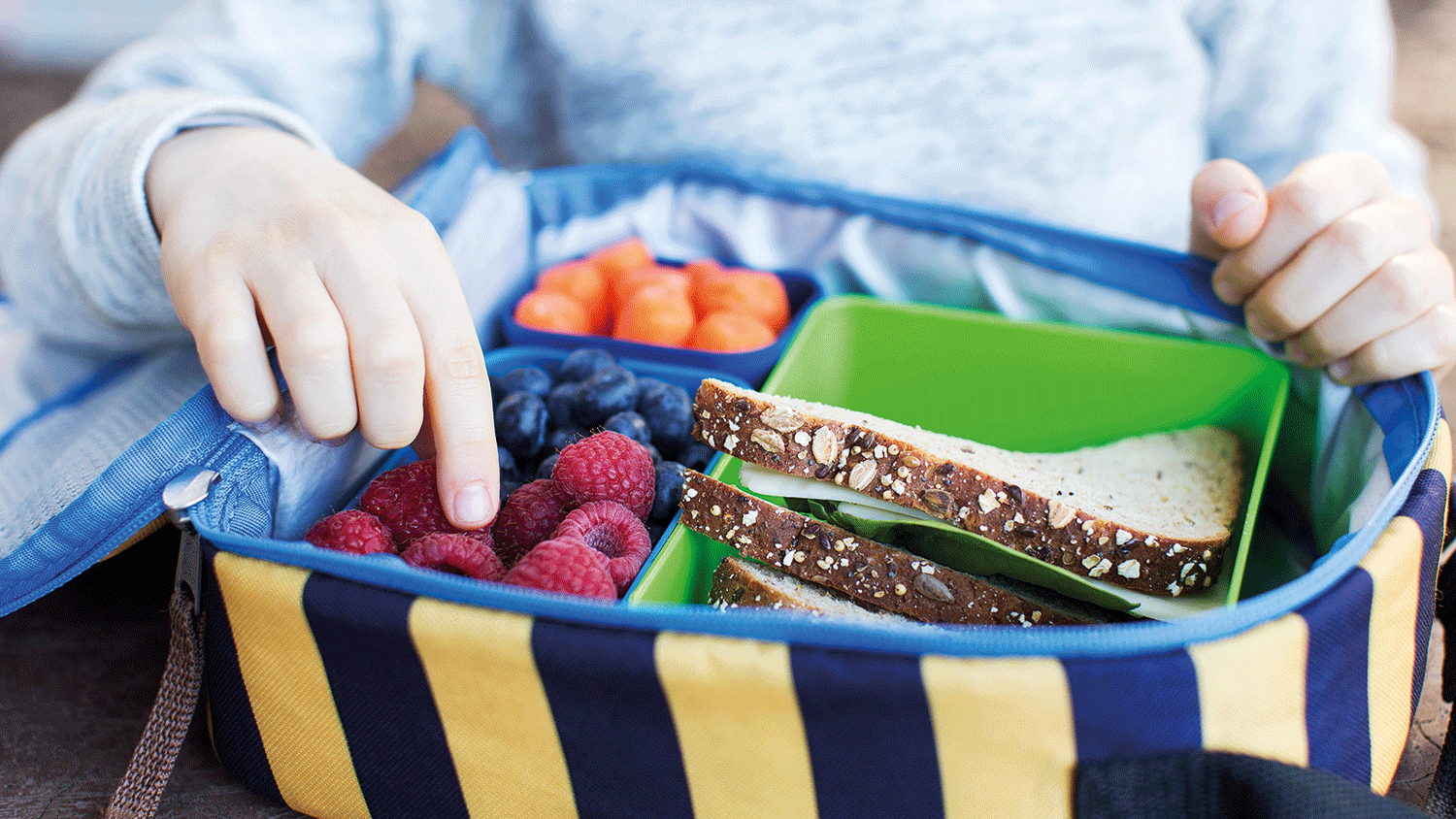 a child picking a fruit in a healthy lunch bag