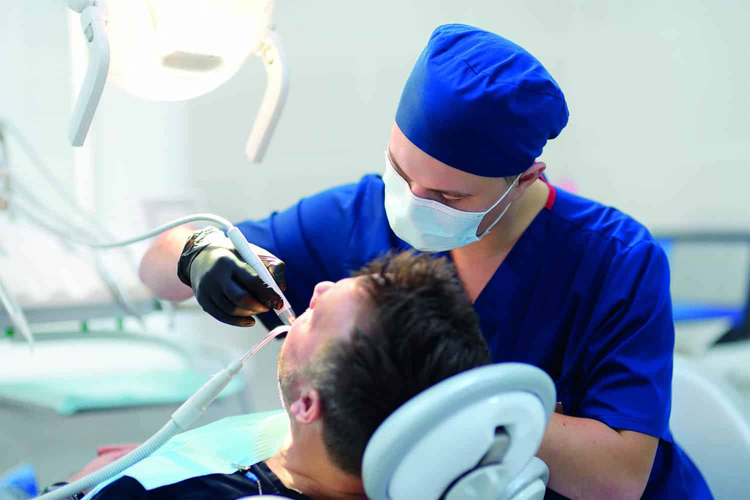 masked dentist examining patient’s teeth