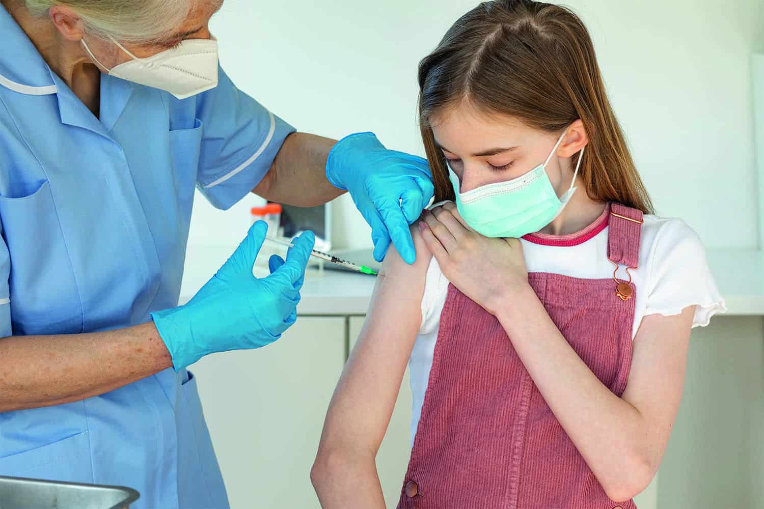 Masked girl receiving vaccination in arm from nurse