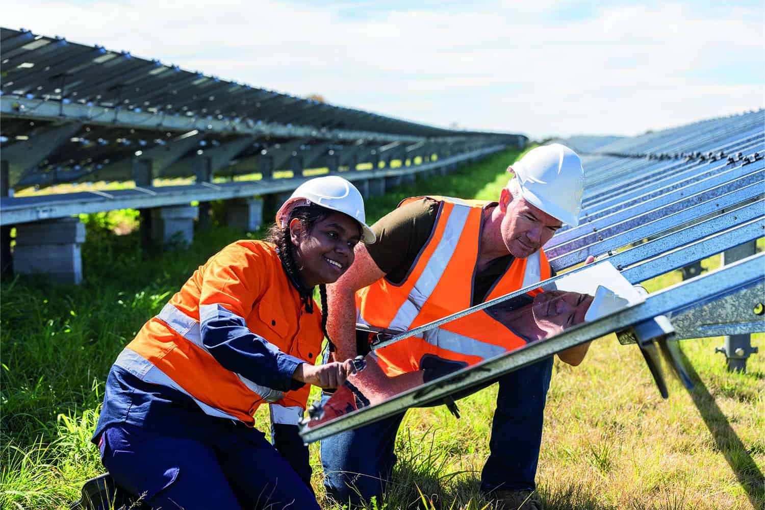 Asian woman and white man in hard hats installing solar panel in field