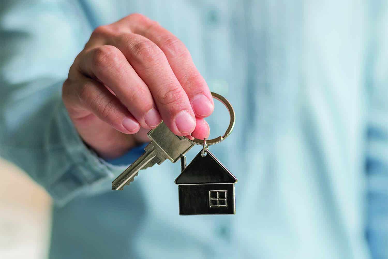 close up of hand holding keyring with house-shaped fob on it