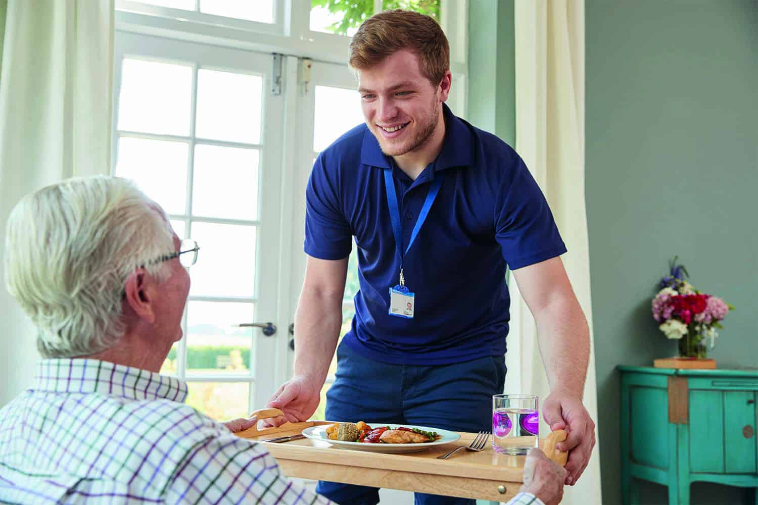 Young male carer giving tray of food to older person