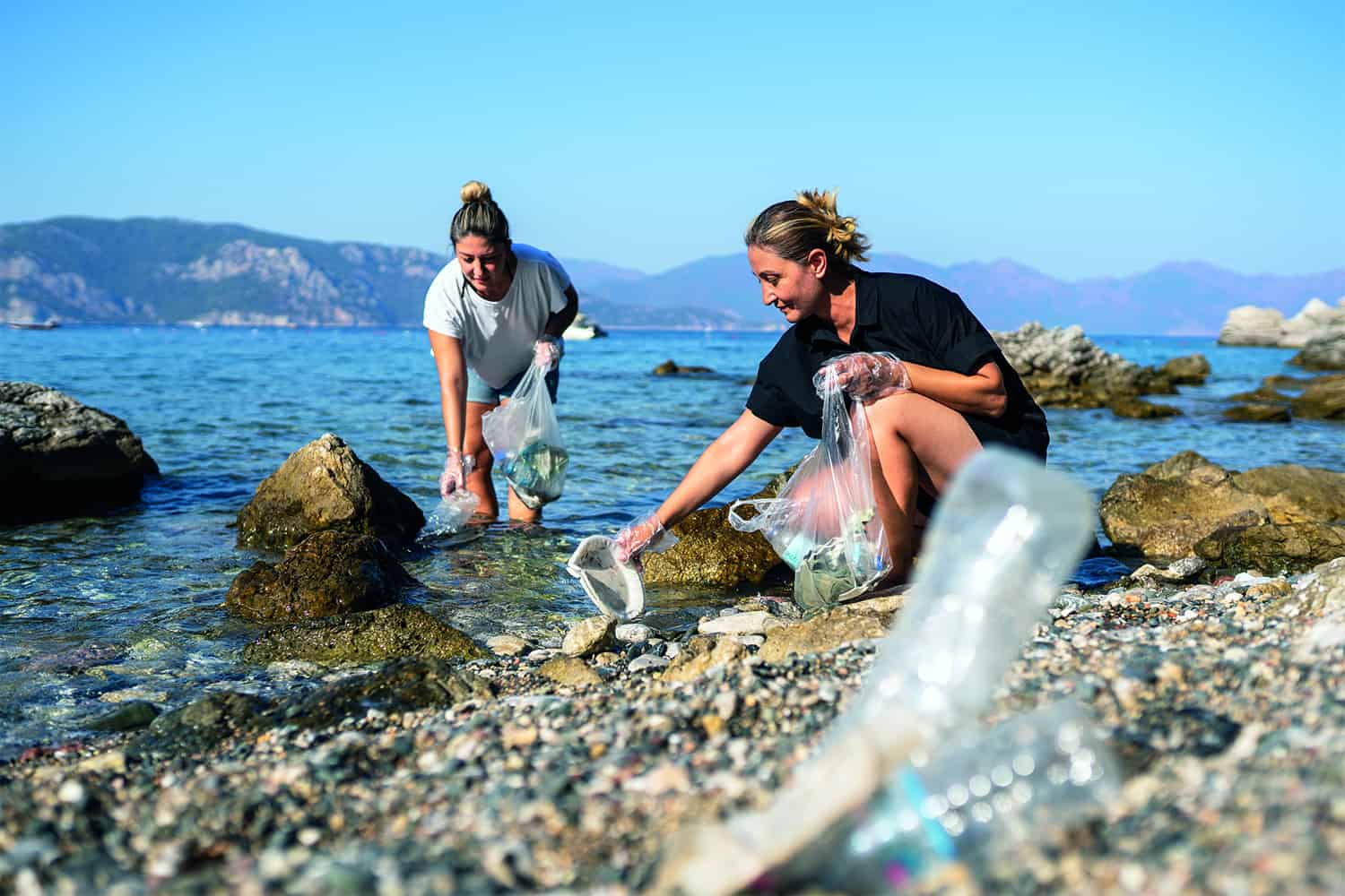 two women picking up plastic waste at shoreline