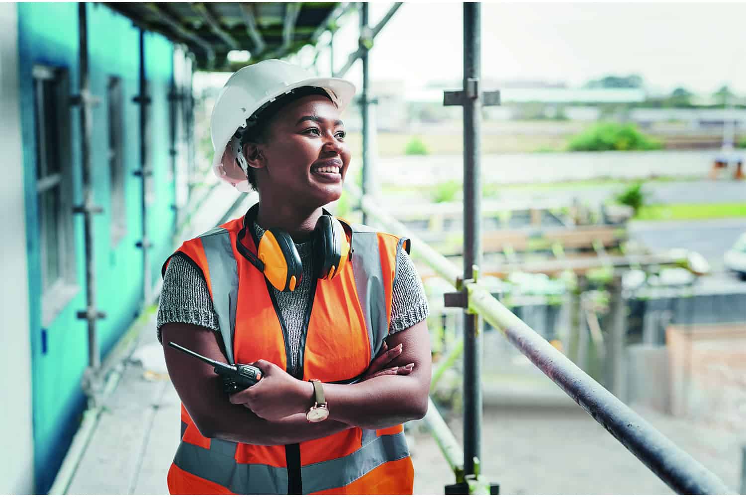 Young woman in builder’s hat and high-vis jacket on building site.