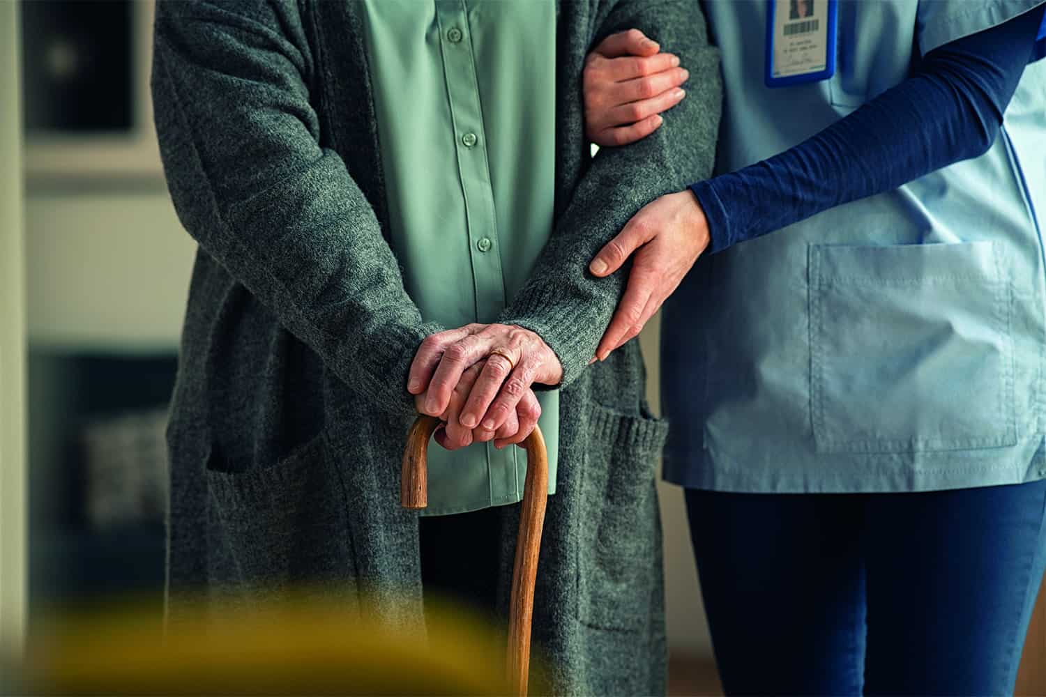 carer supporting older person leaning on walking stick