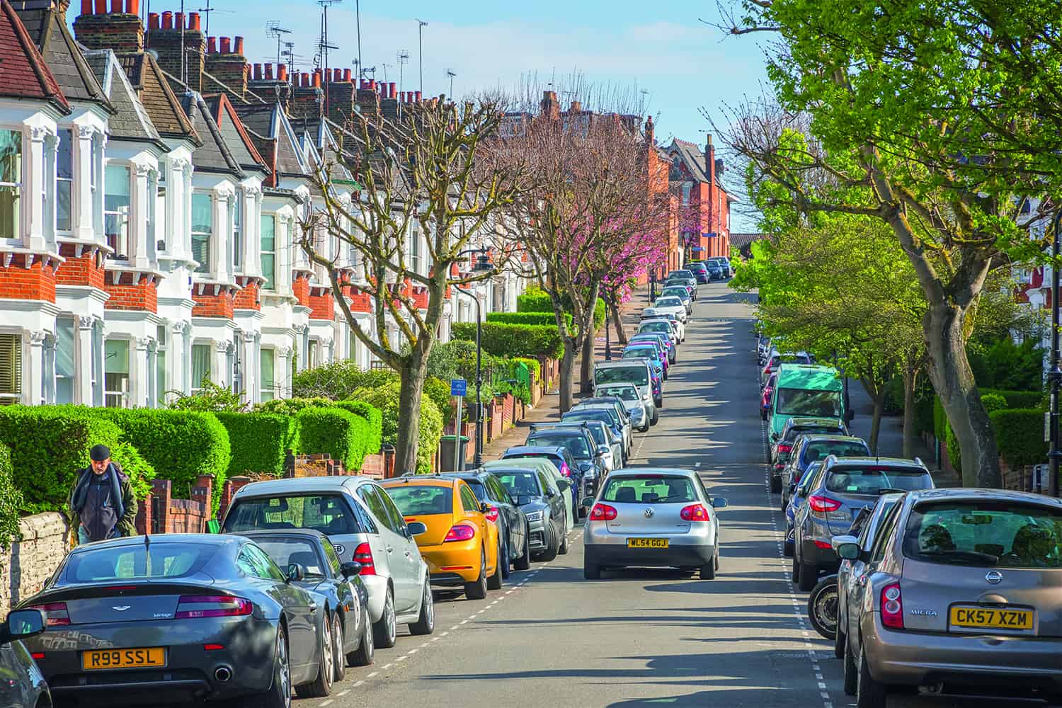 car driving down residential London street between parked cars.