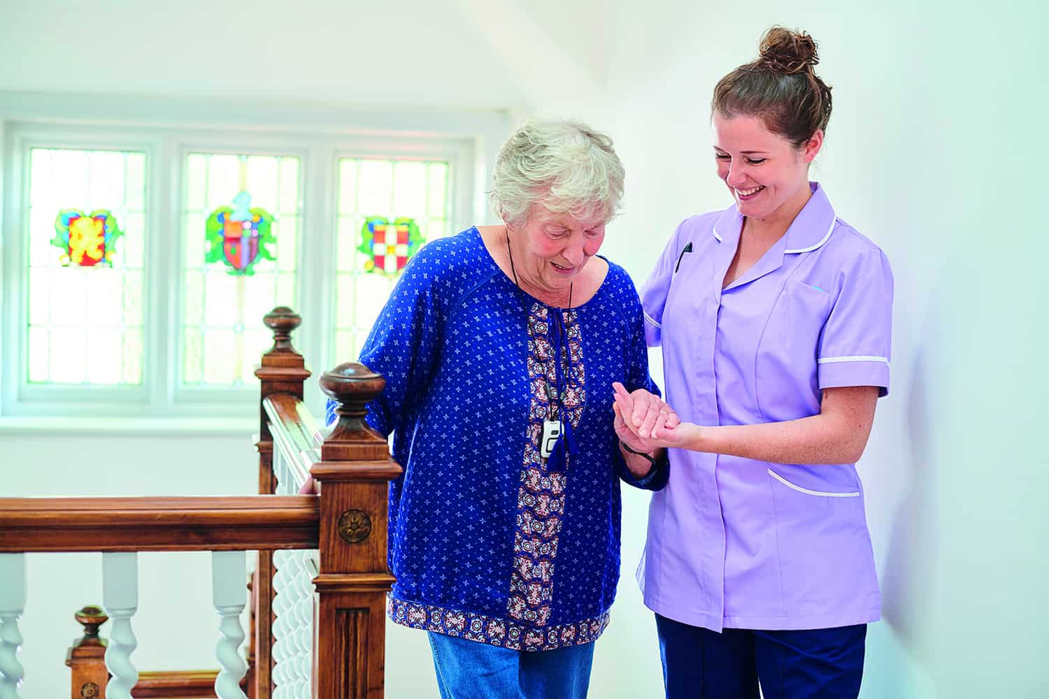 : female carer helping older woman on walking stick.