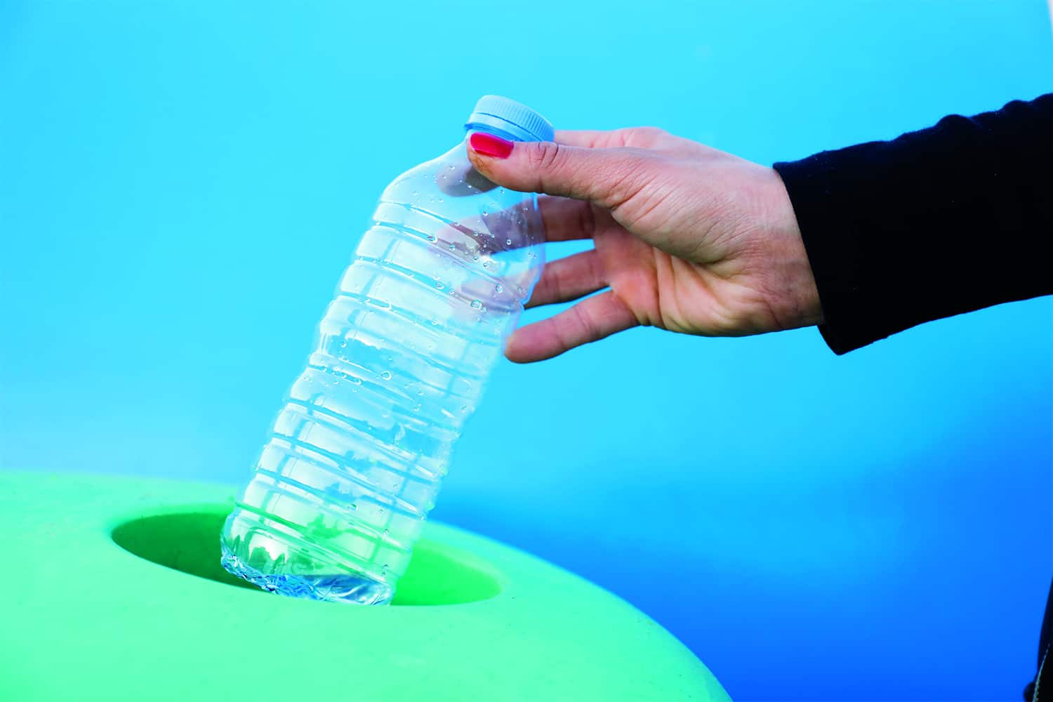hand placing plastic bottle in green bin