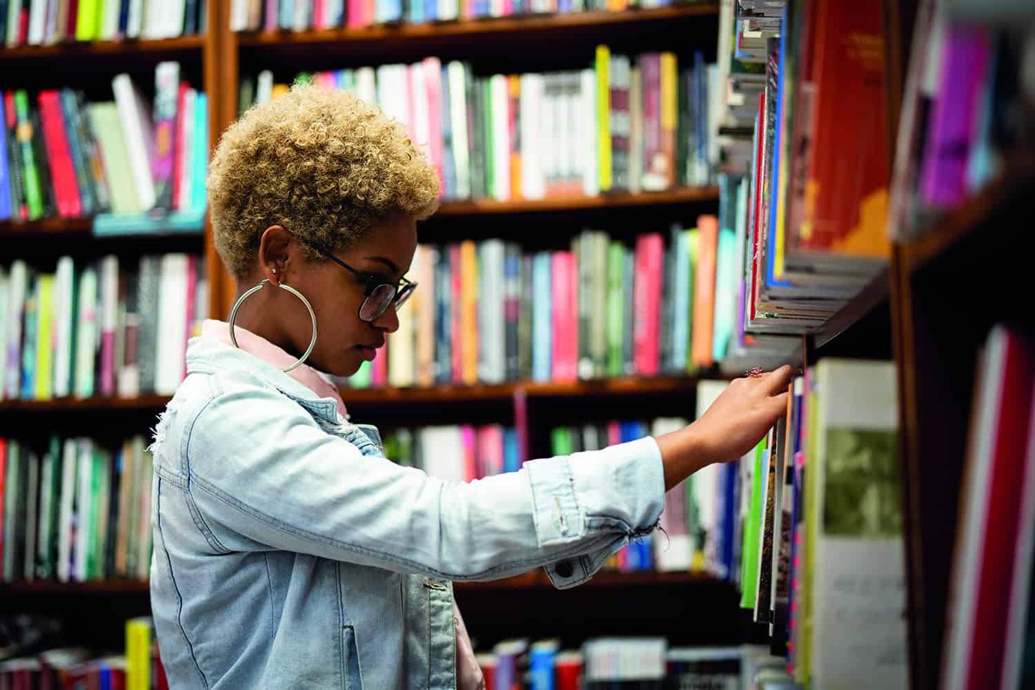 A black woman in a library looking at books.
