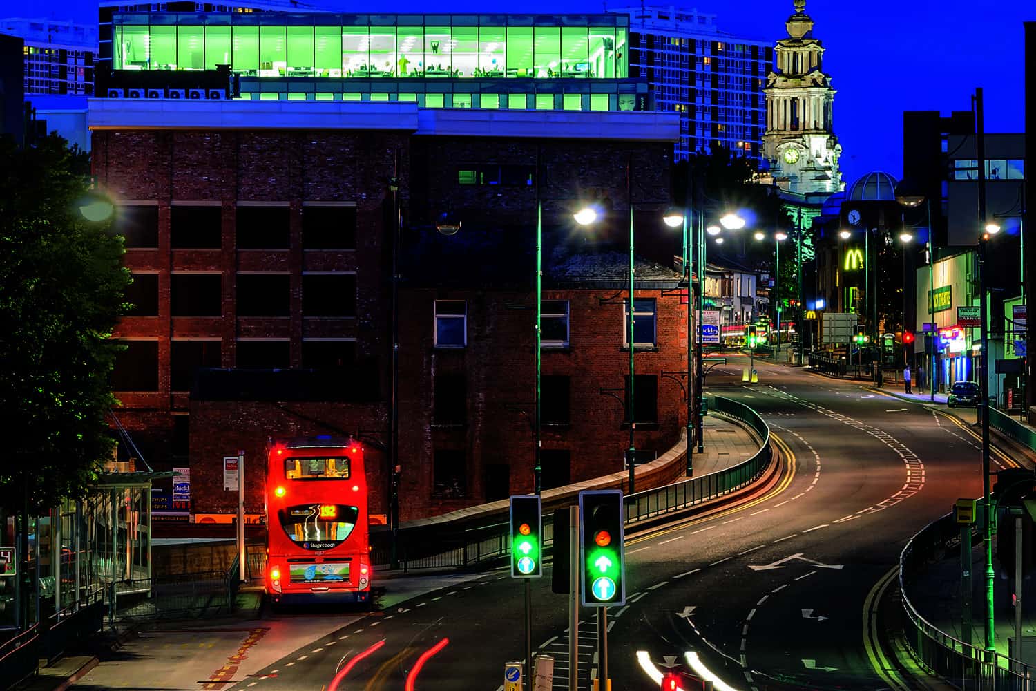 A bus travelling through a high street at night.