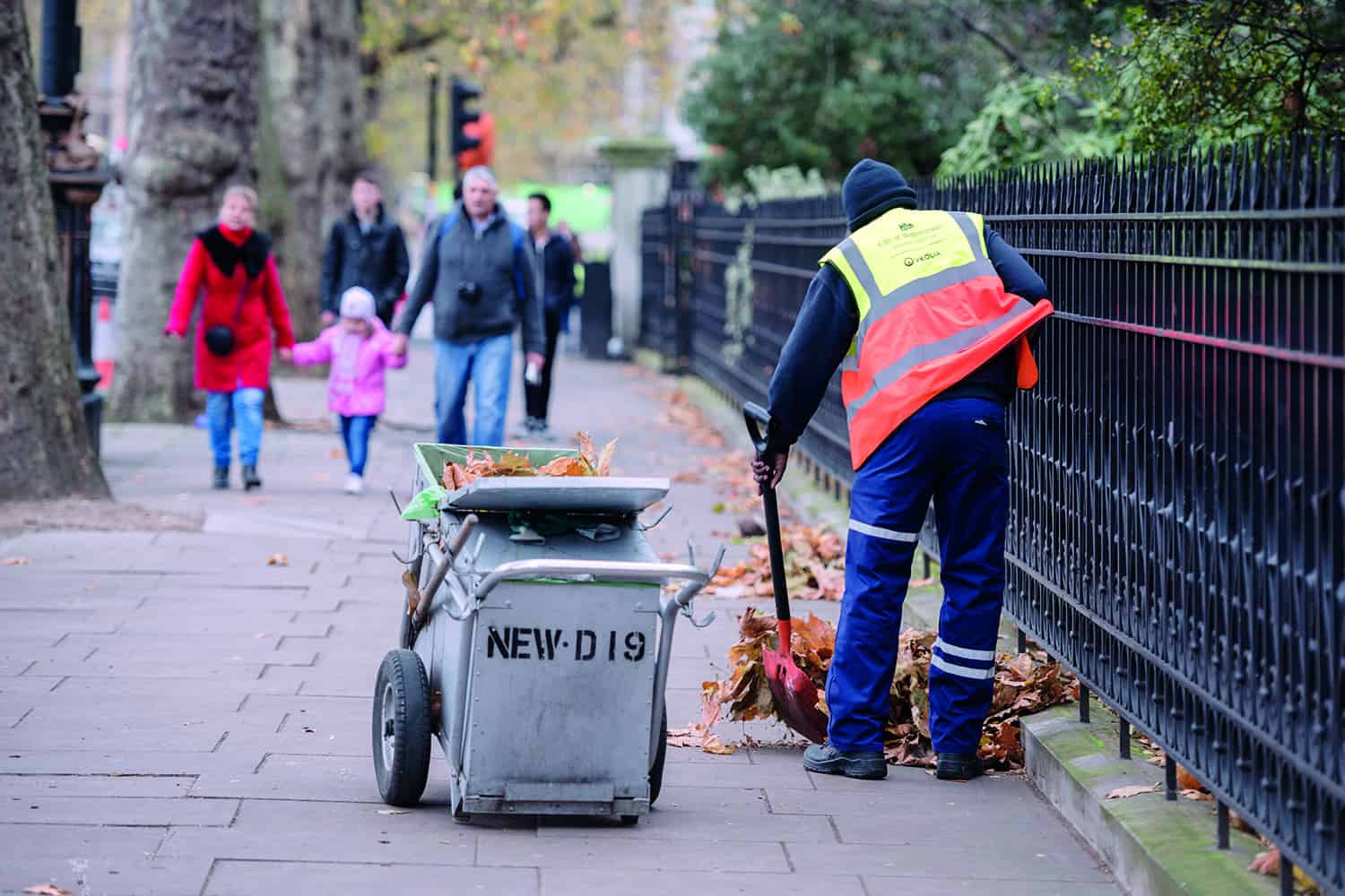 A council worker sweeping dead leaves off the street.