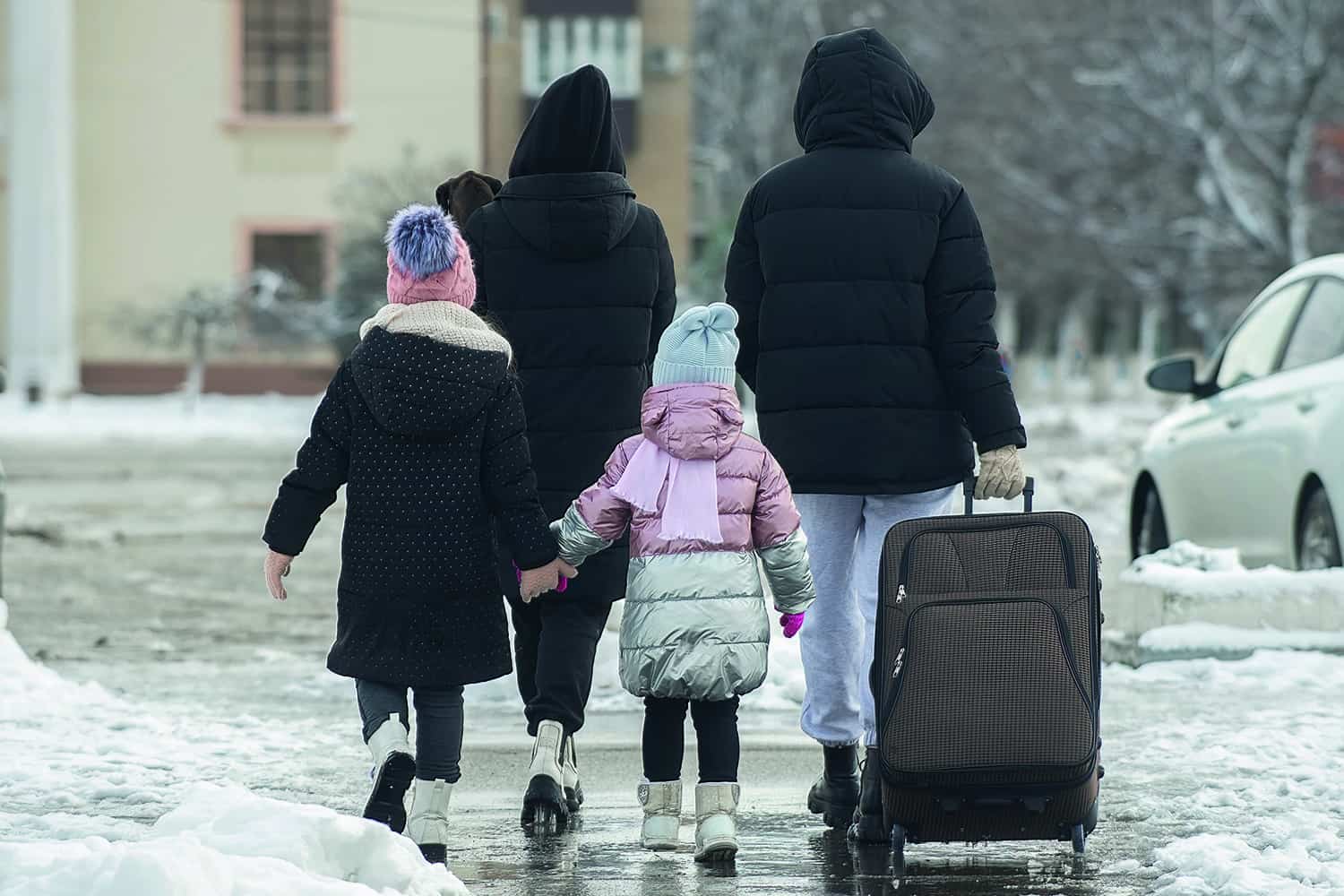 A family walking in the snow pulling a suitcase.