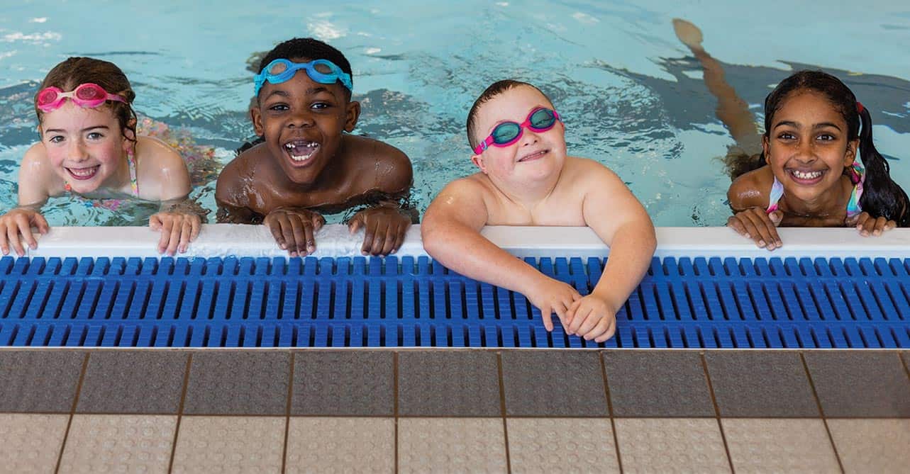 four young children smiling from the water at the edge of a swimming pool