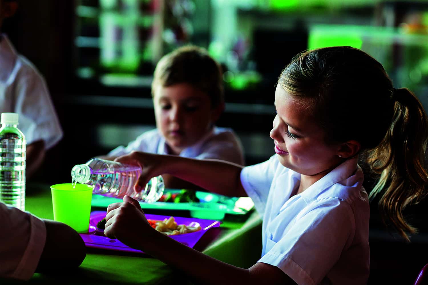 Young girl and boy eating school dinner off plastic trays.