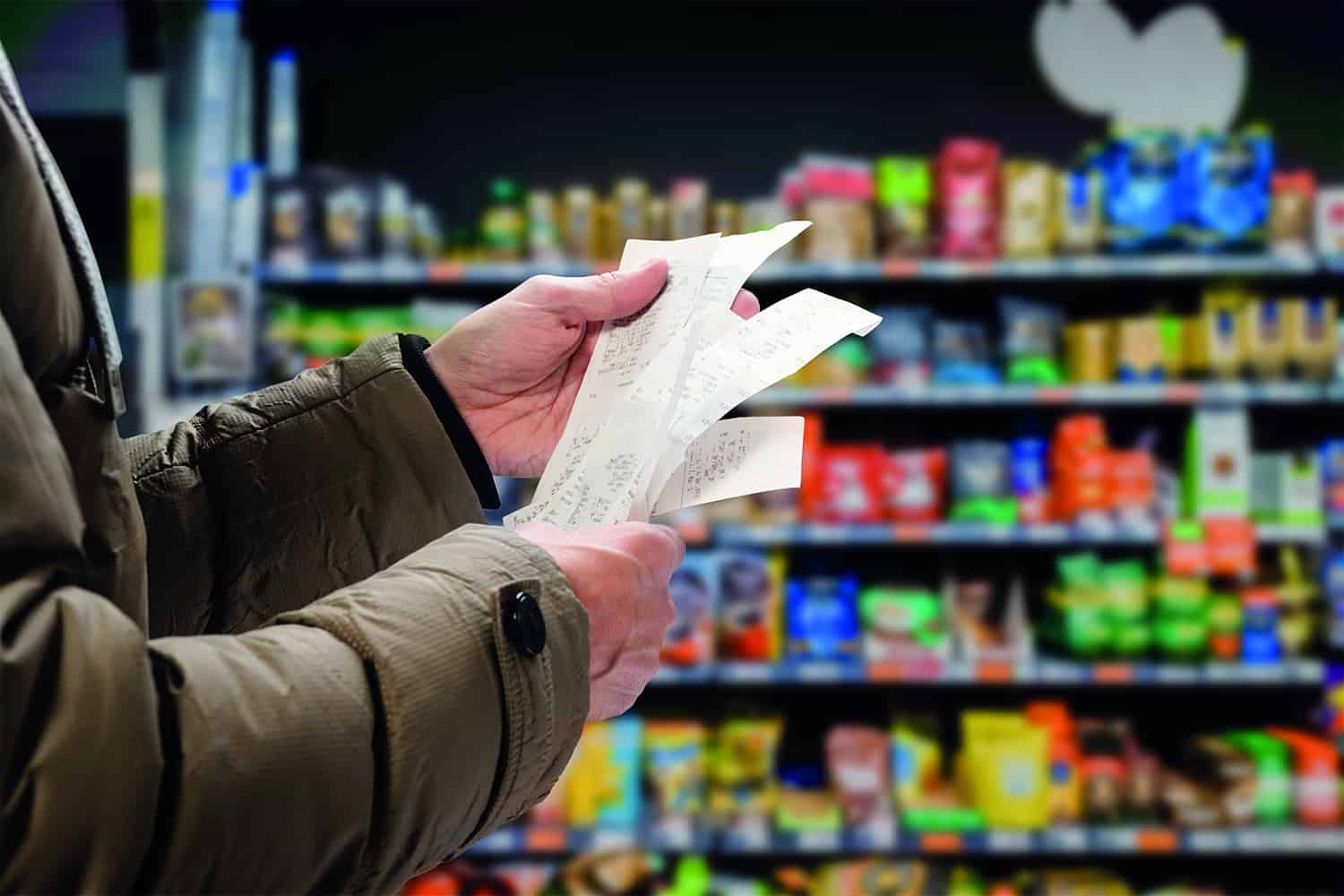 Close-up of man holding shopping receipts in supermarket aisle.