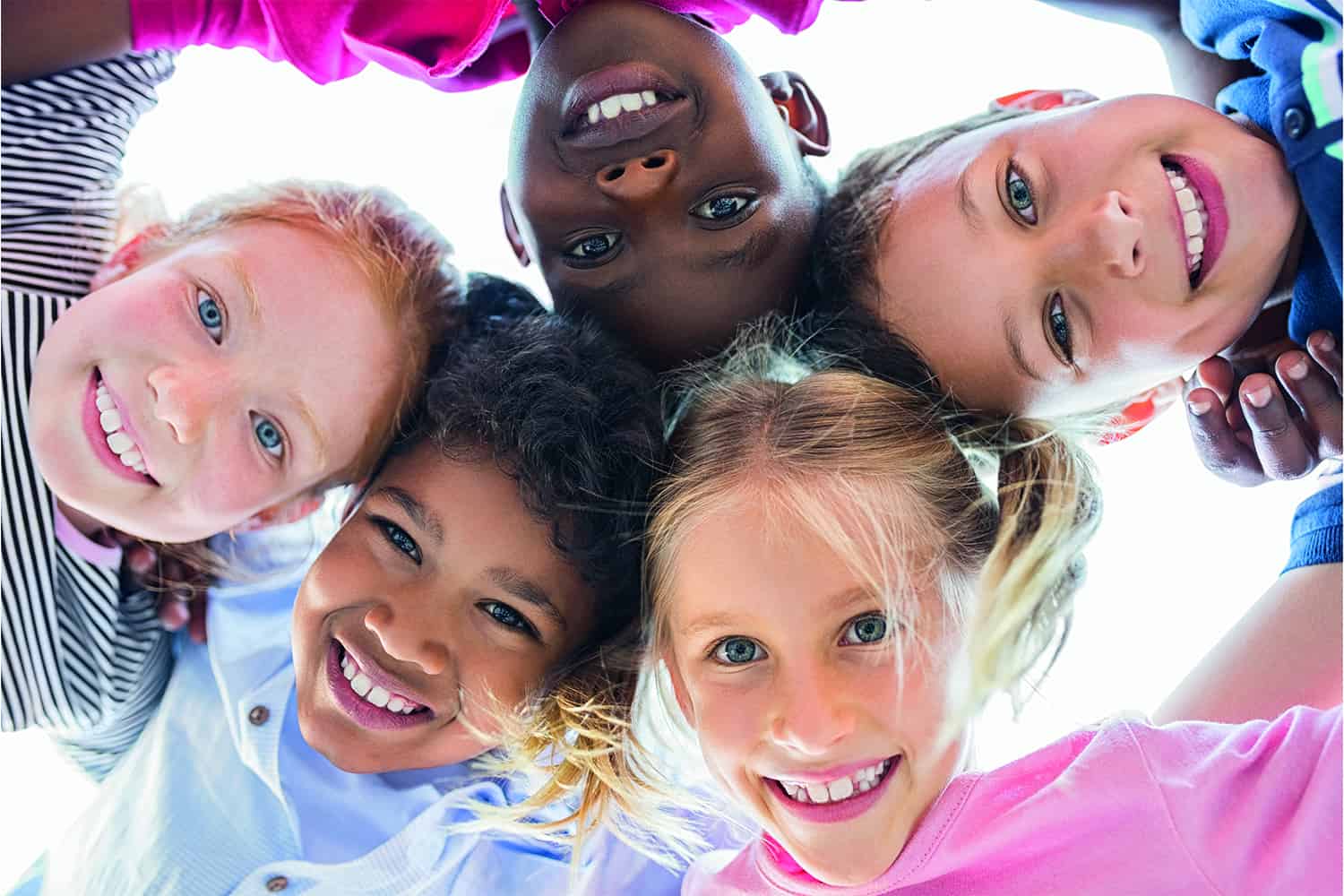close-up of diverse group of children in linked circle looking down at camera