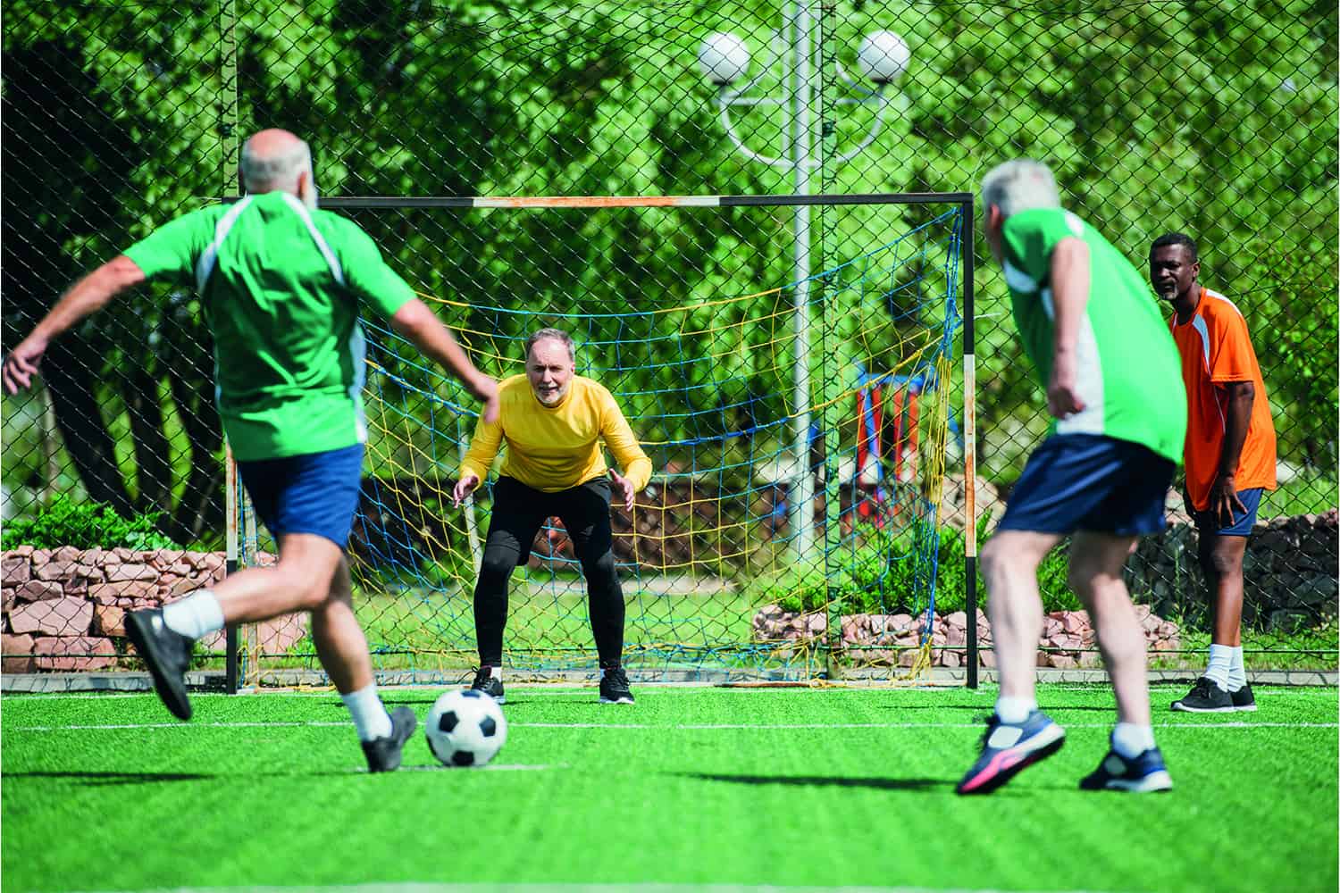 older man shooting football at goalkeeper.