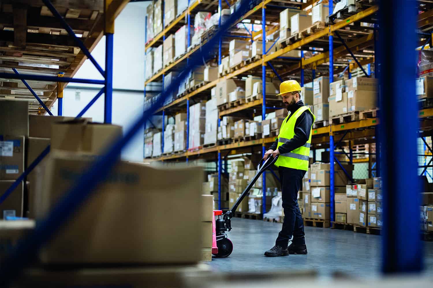 warehouse worker in high vis and headgear using trolley to move products