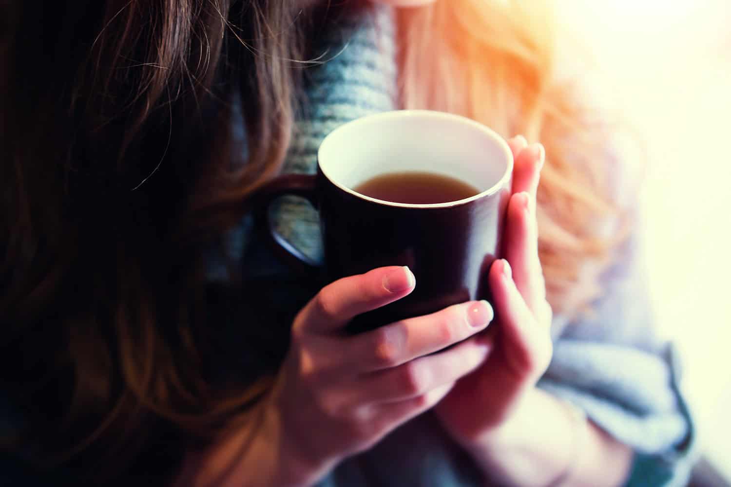 woman in warm jumper holding mug of coffee
