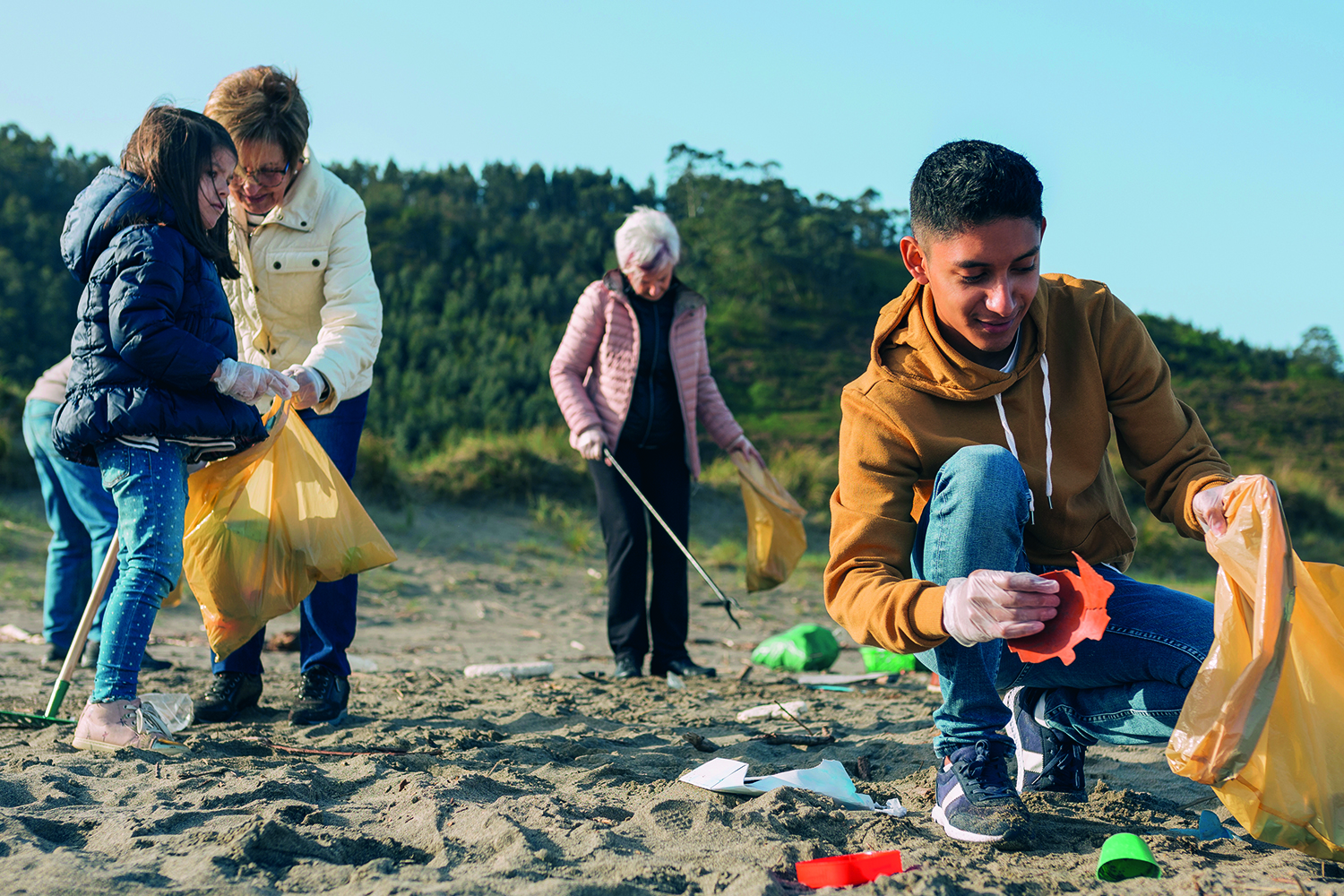 close-up of young person on beach putting litter in a rubbish bag, older woman behind with litter picker and stick. Second pic: woman volunteer handing donations to older woman.
