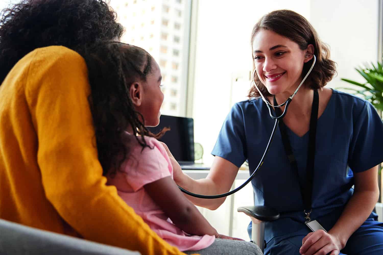 photo of female health worker using stethoscope on young girl sitting on mum’s lap