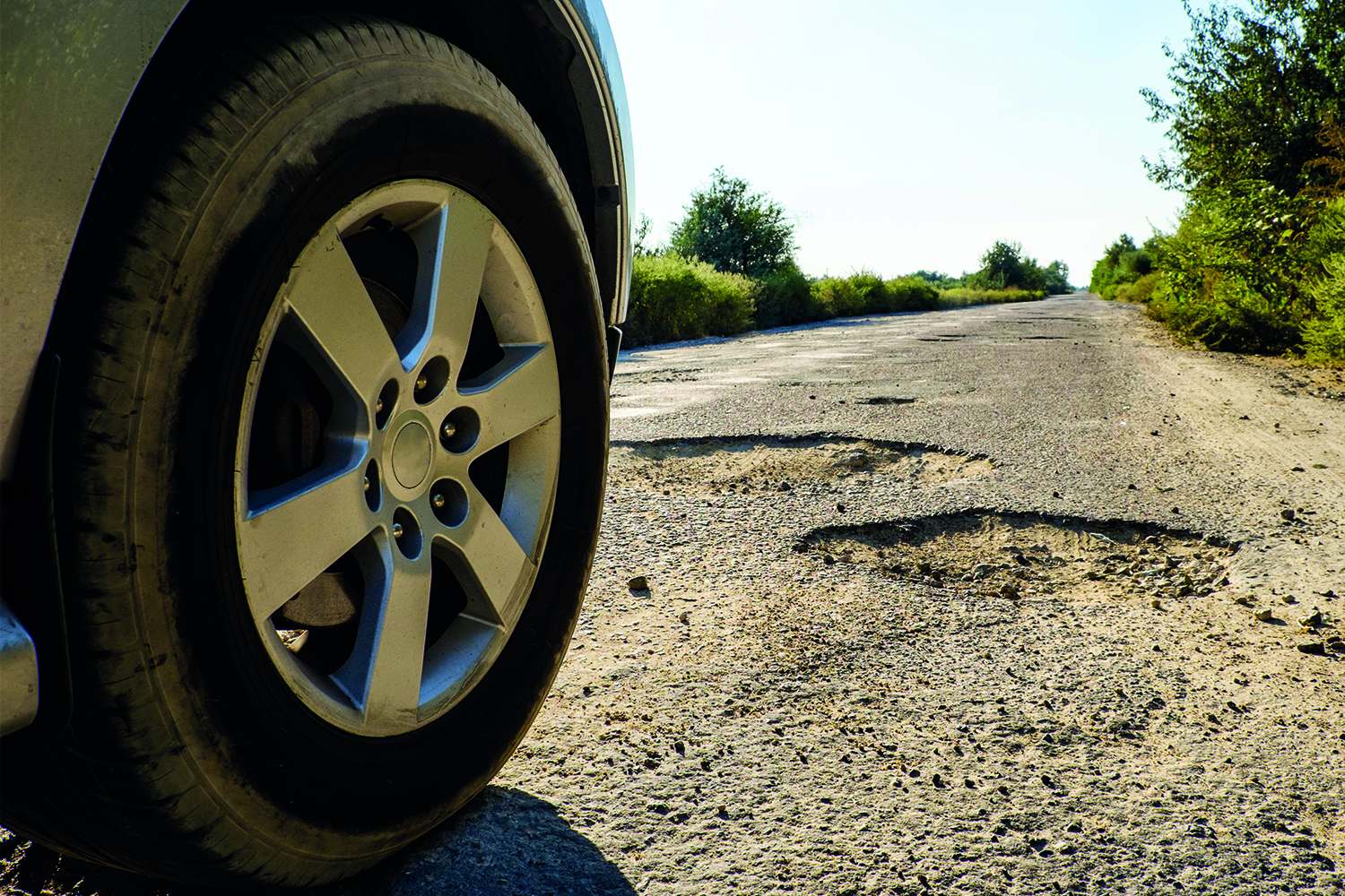 low-down close-up of car wheel and front of car driving along potholed lane