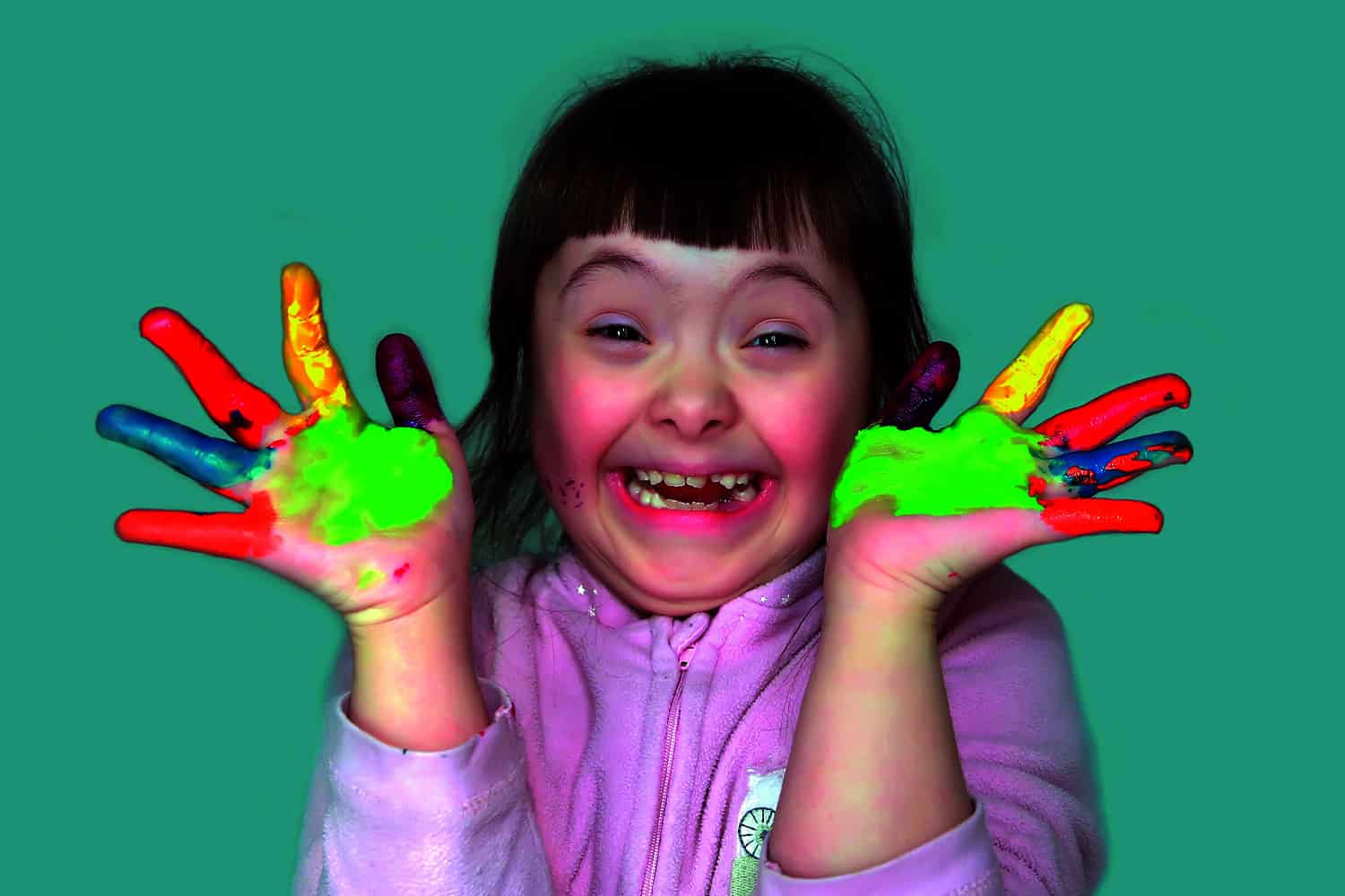 smiling girl with Down Syndrome, hands and fingers painted in different colours.