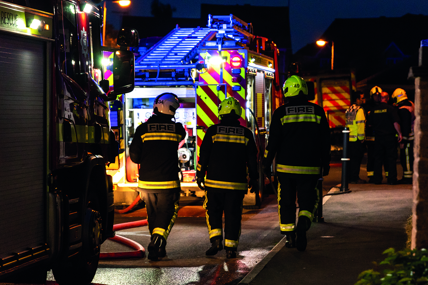 Three firefighters walking towards a fire engine at night