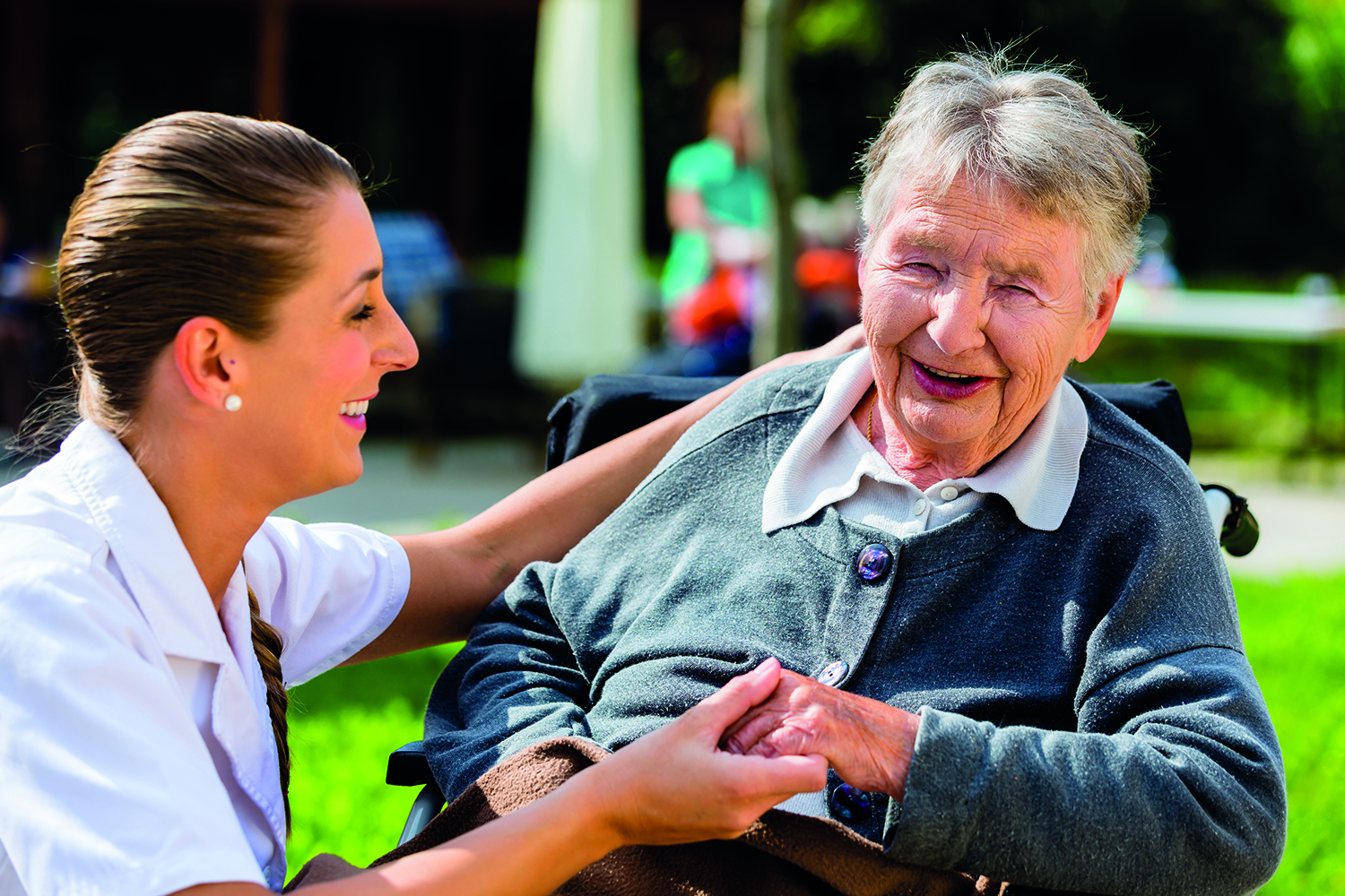 A smiling care worker holding hands with an older women in a chair