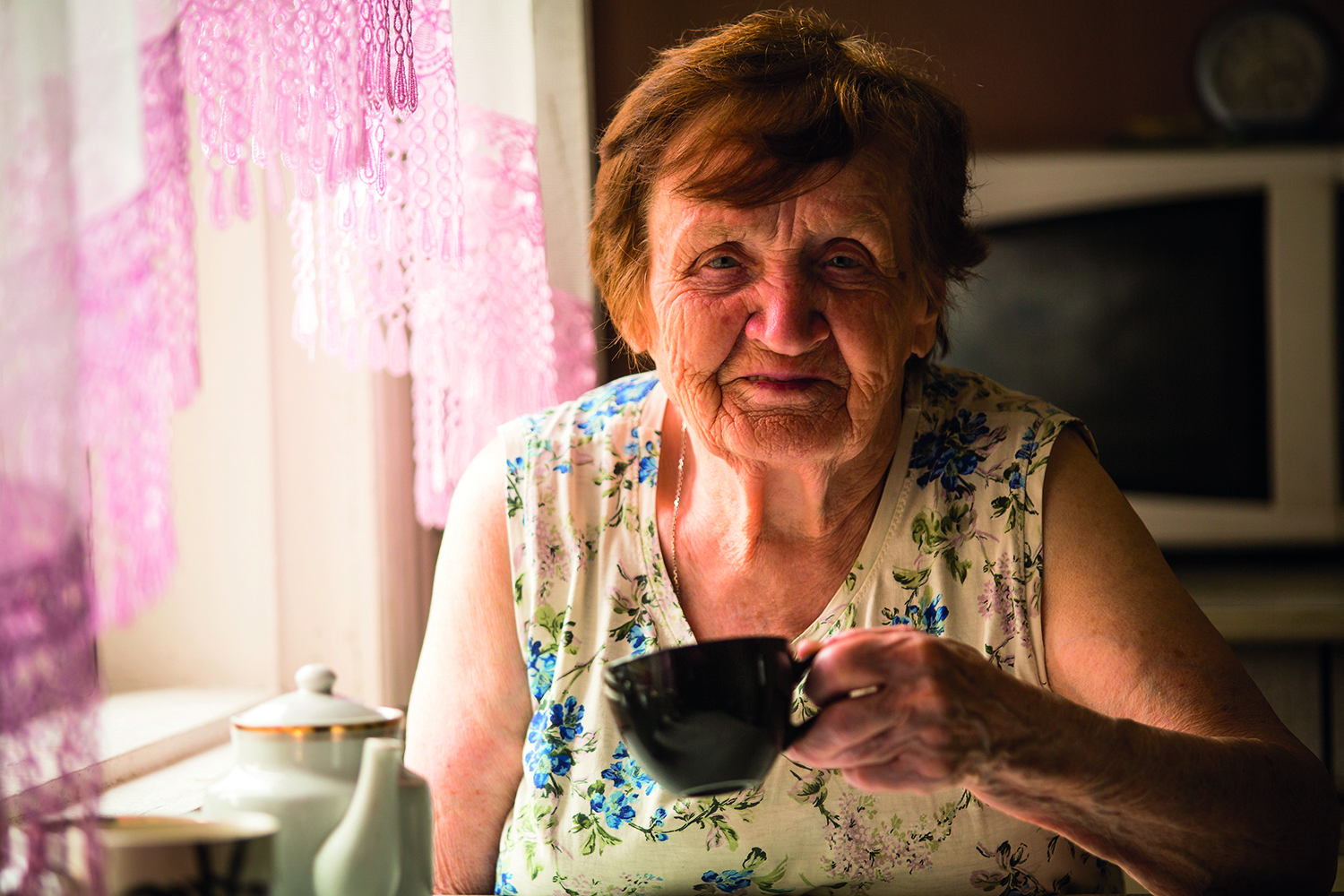 Elderly woman holding a cup in hand.