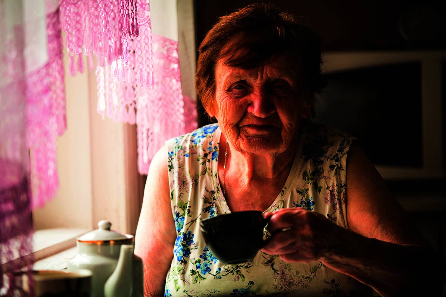 Elderly woman holding a cup in hand.