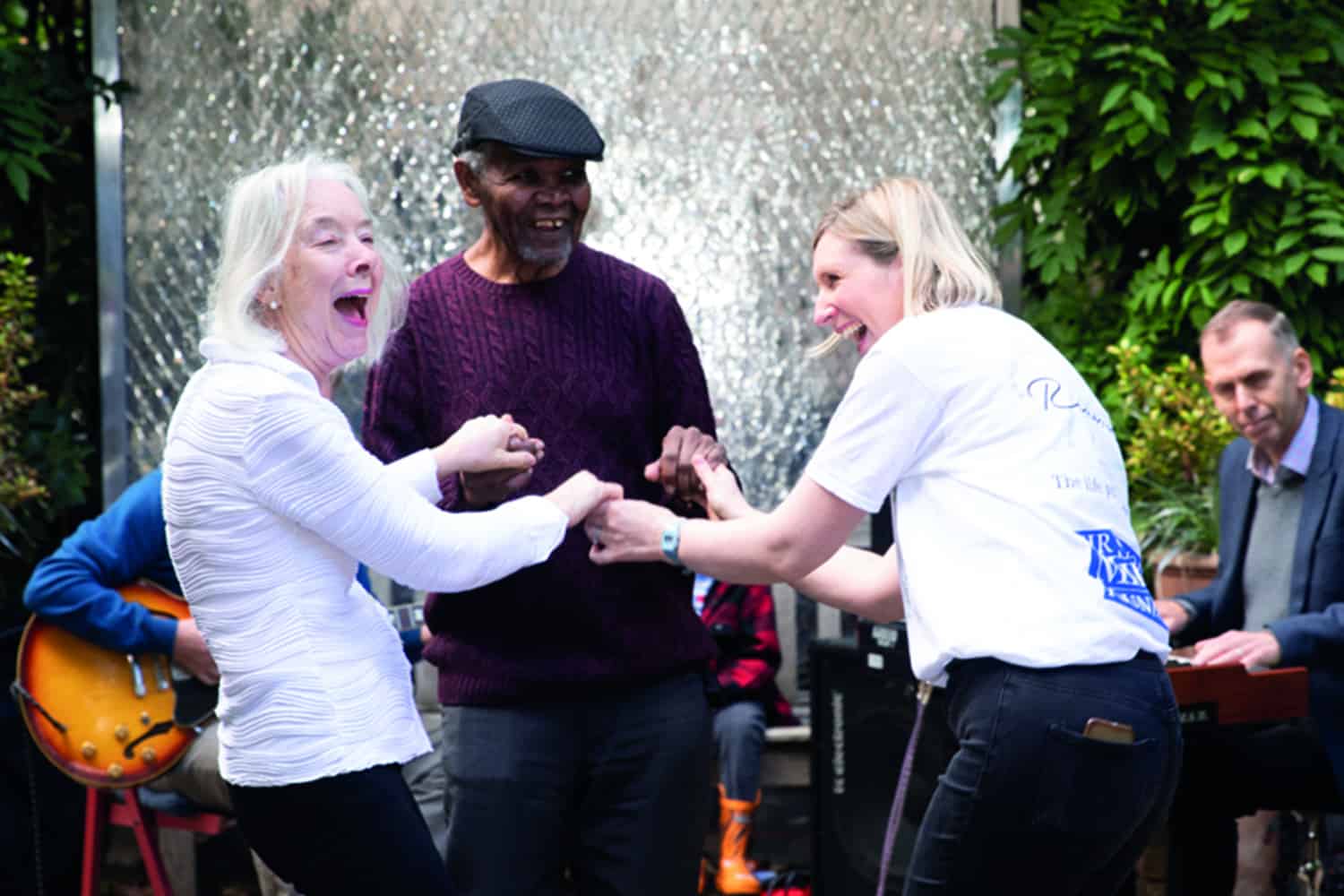 An elderly lady and man dancing with a volunteer at a Silver Sunday afternoon tea party