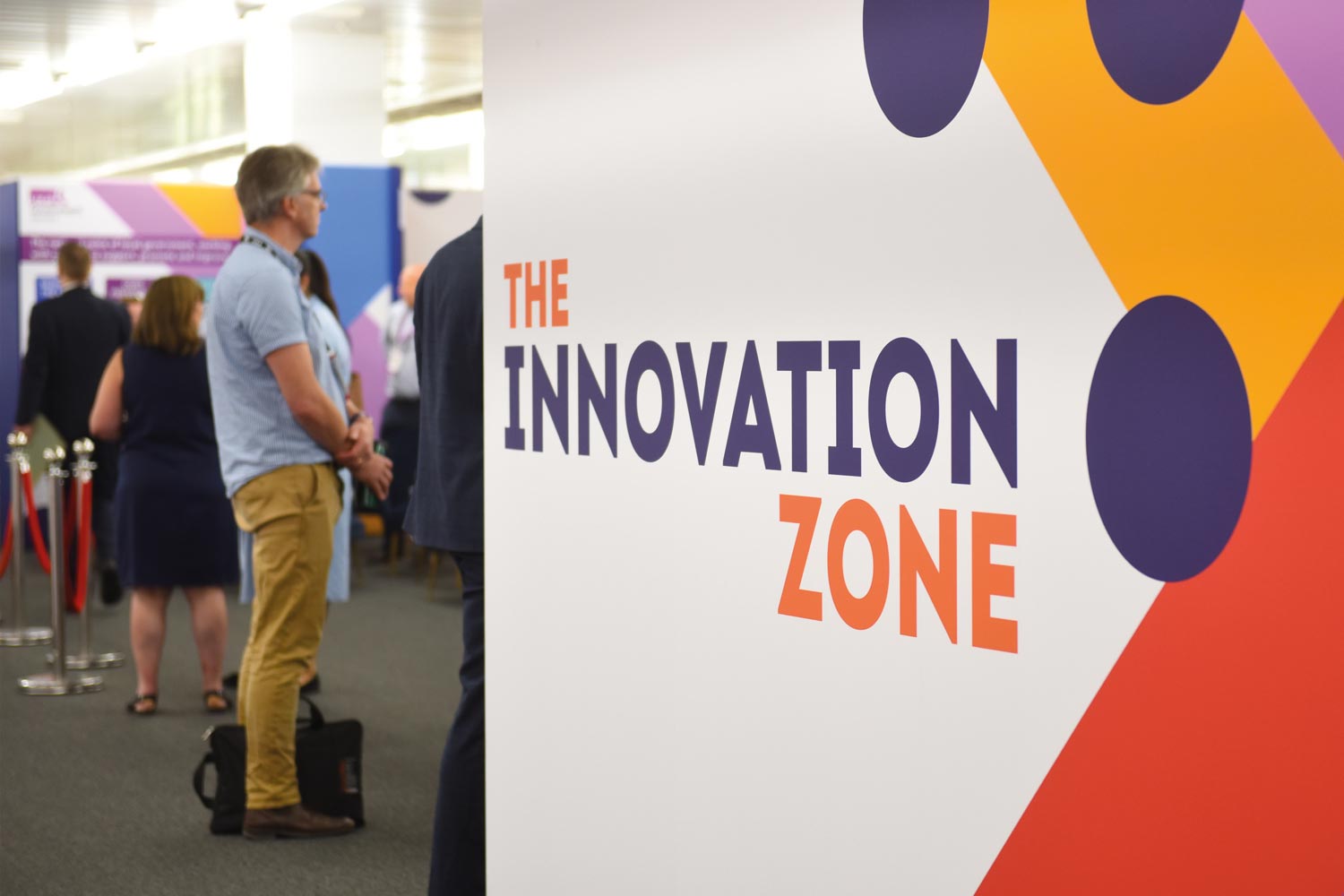 A sign saying The Innovation Zone in a conference hall with delegates mingling nearby