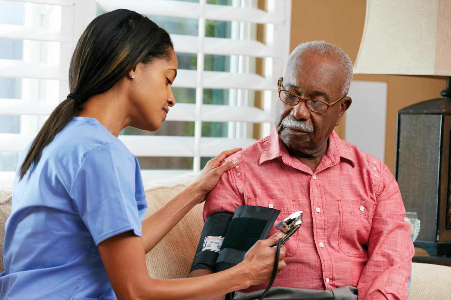 Black female nurse taking blood pressure of black male patient.