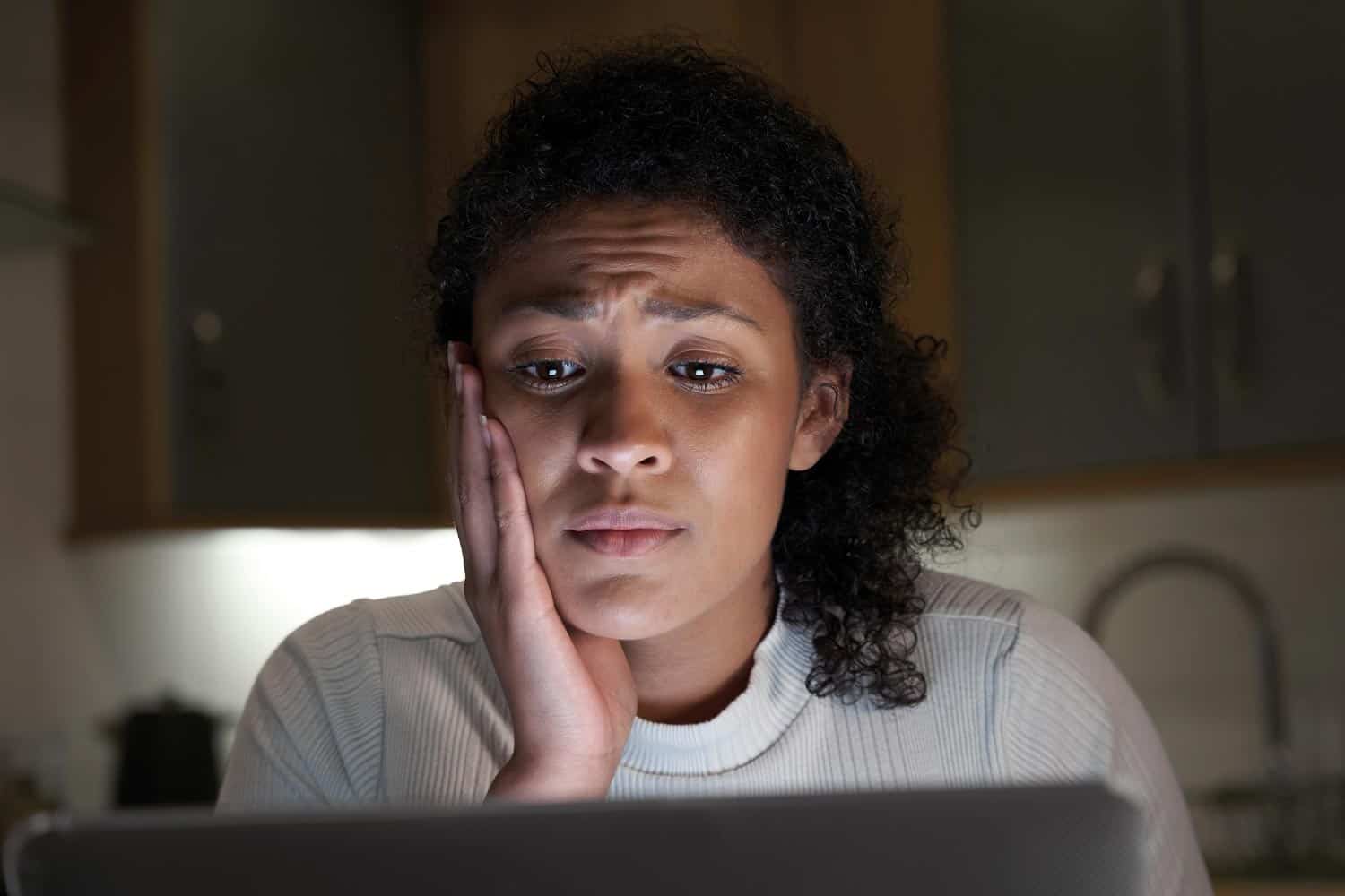 A young woman in front of a computer screen looking anxious.