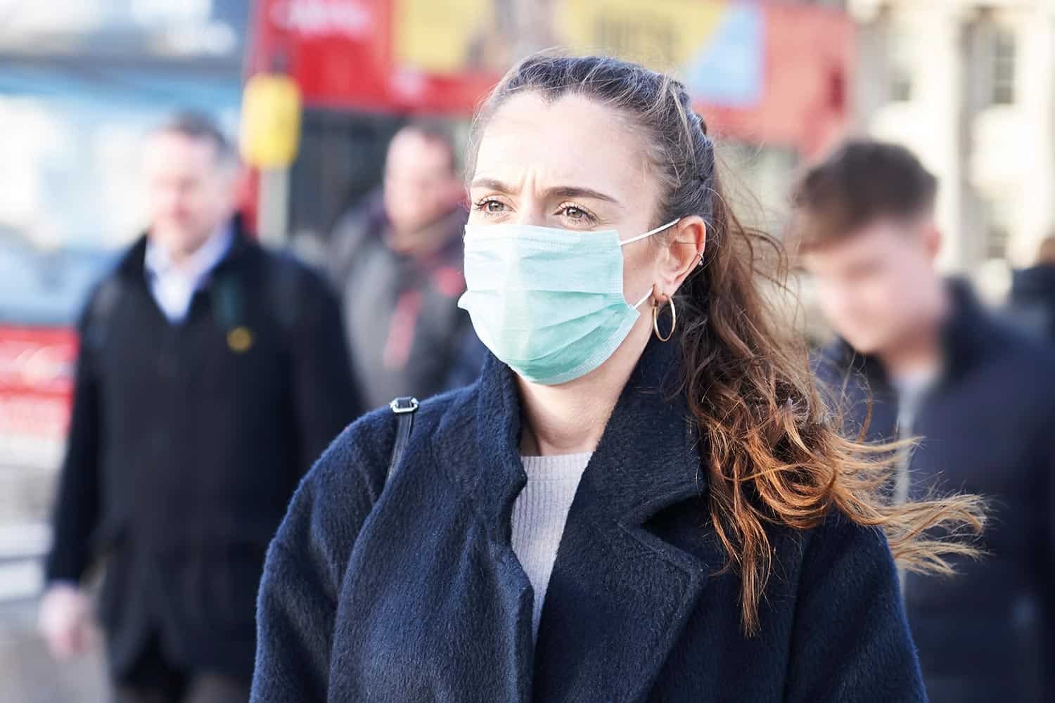 A woman wearing a coat and a mask on face.