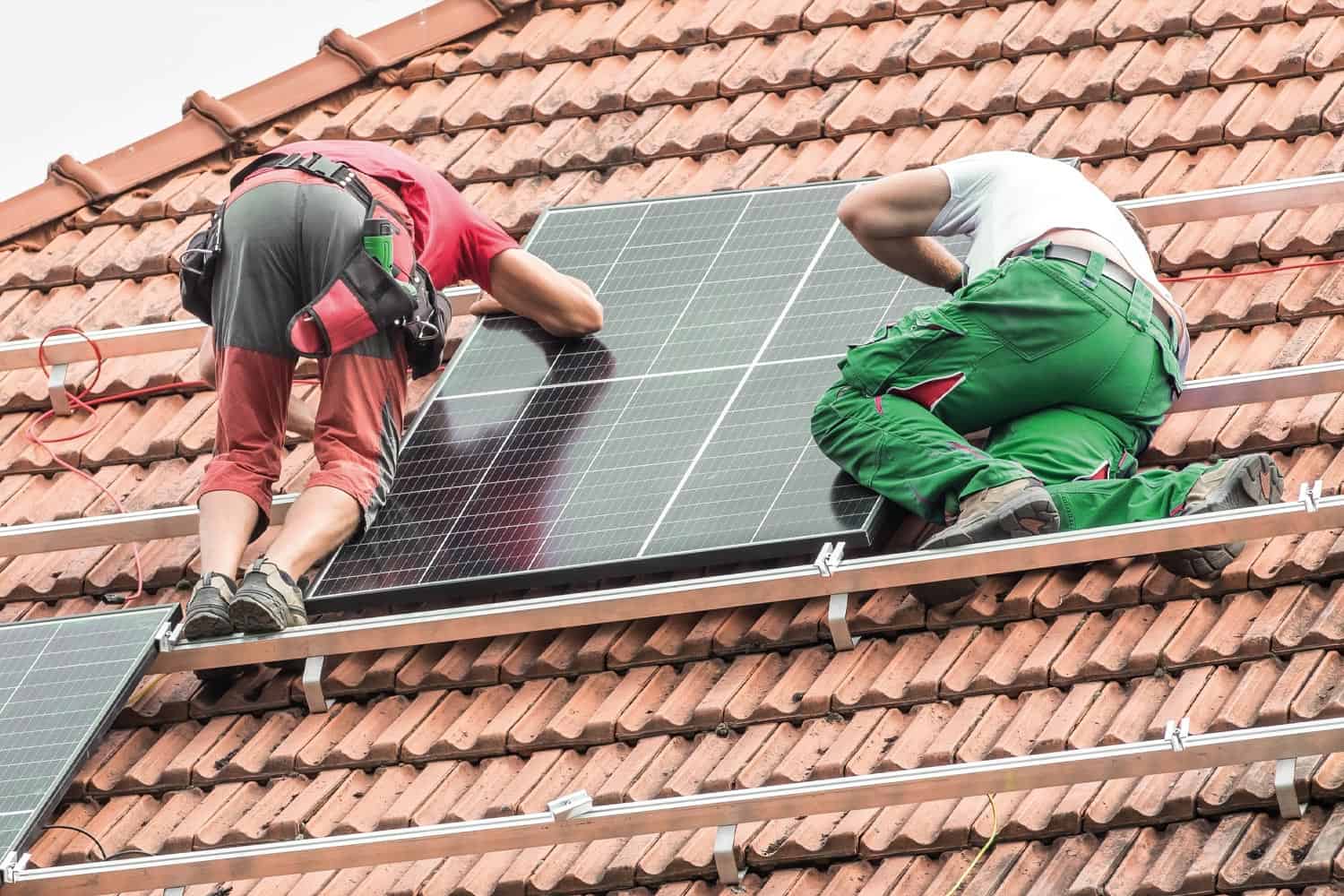 Two workmen on a roof installing a solar panel