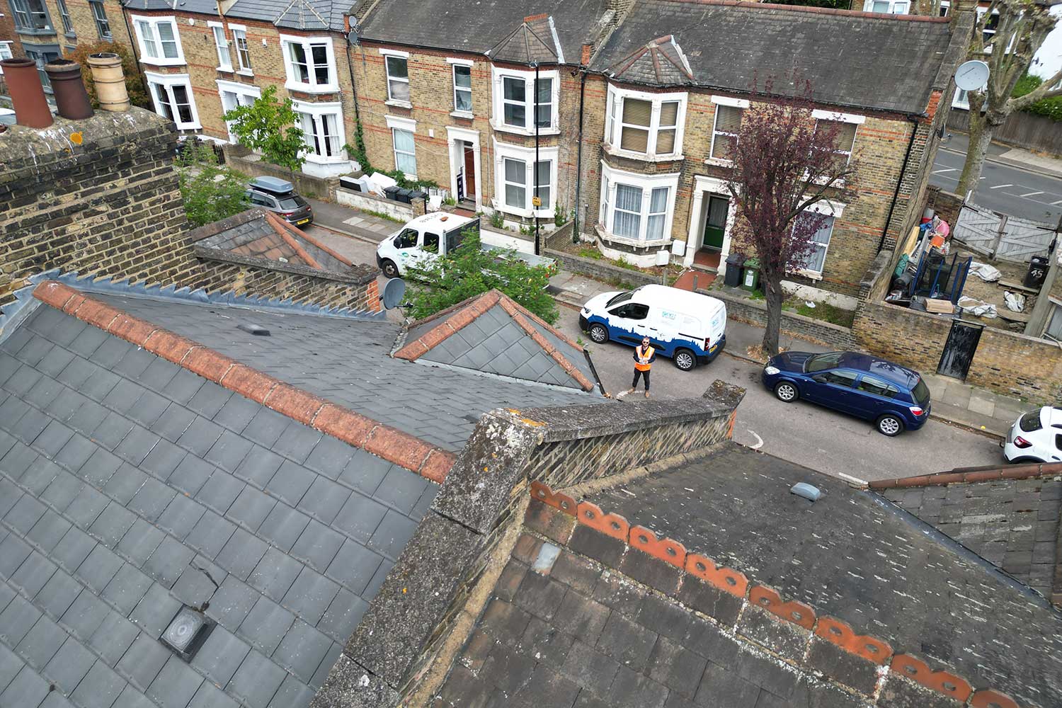shot from drone hovering above the roof of a house looking down at the drone operator in the road below