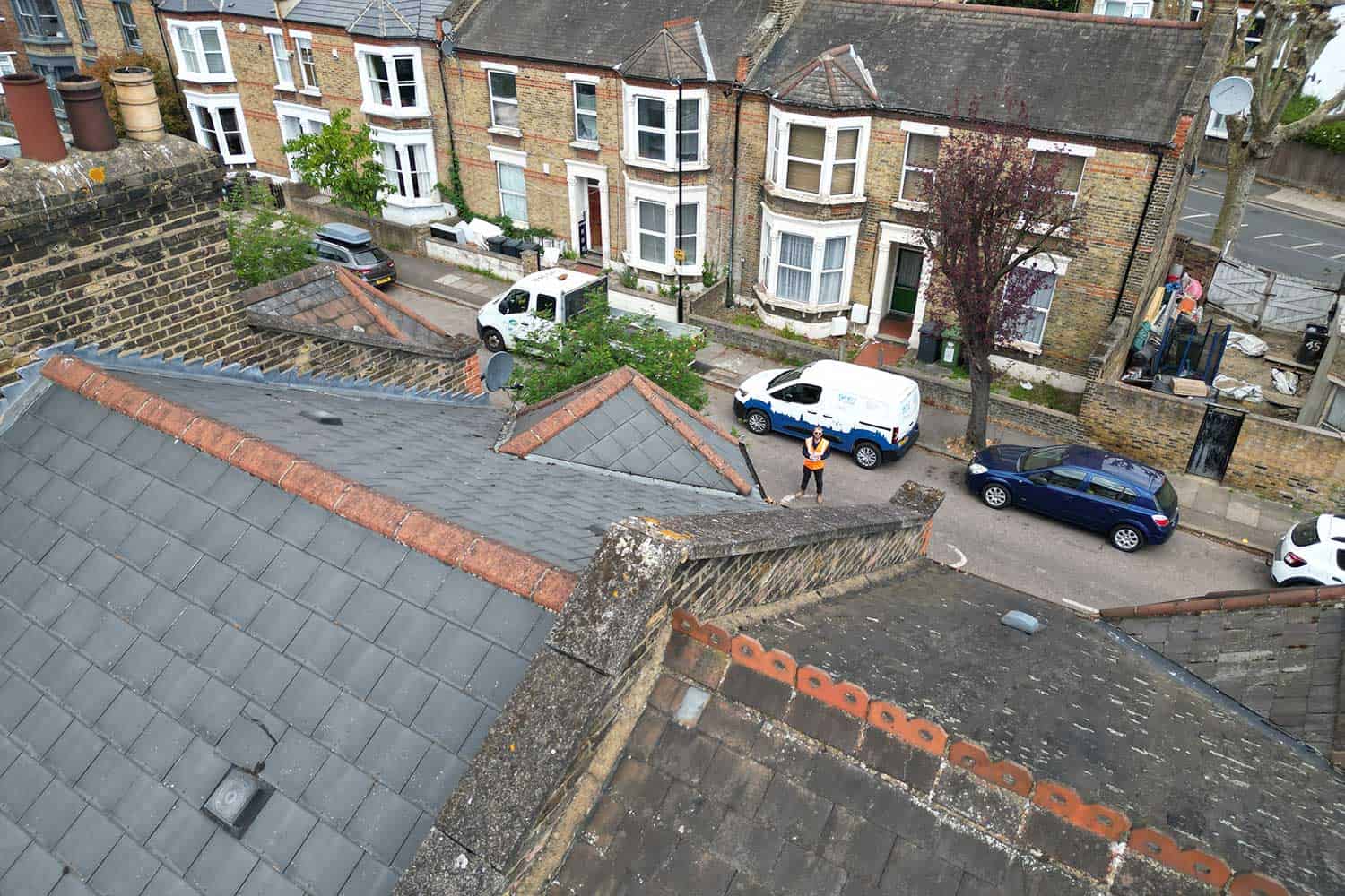 shot from drone hovering above the roof of a house looking down at the drone operator in the road below