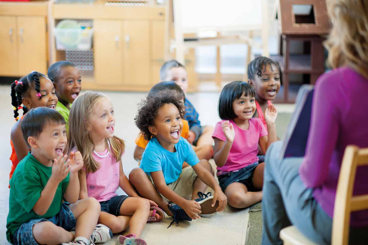 A teacher sat with a group of nursery kids.