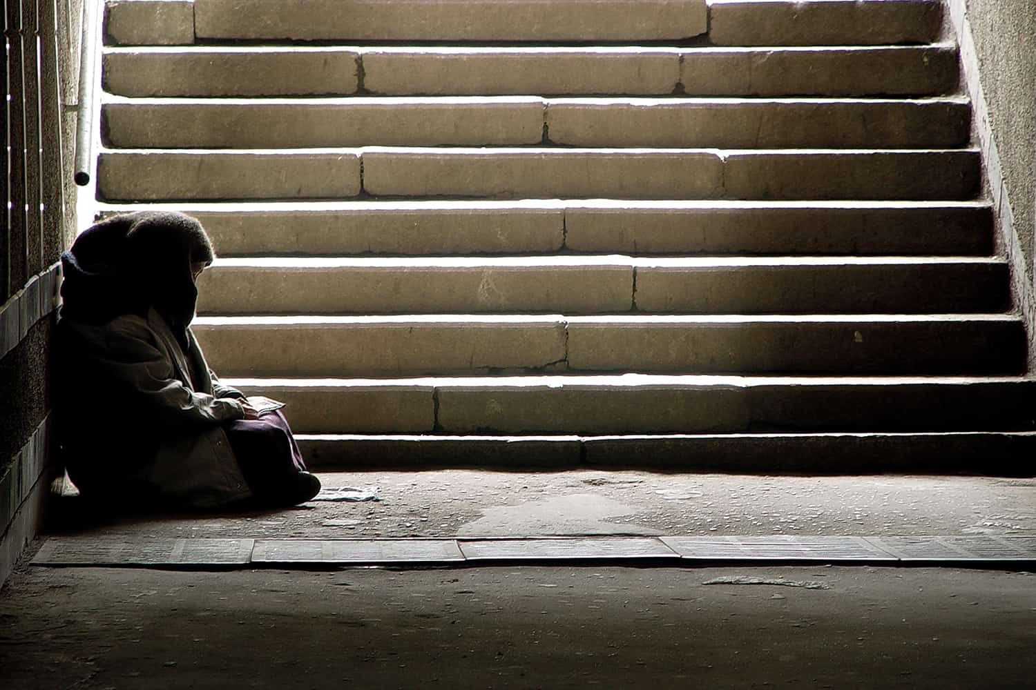A homeless person sat below a set of stairs.