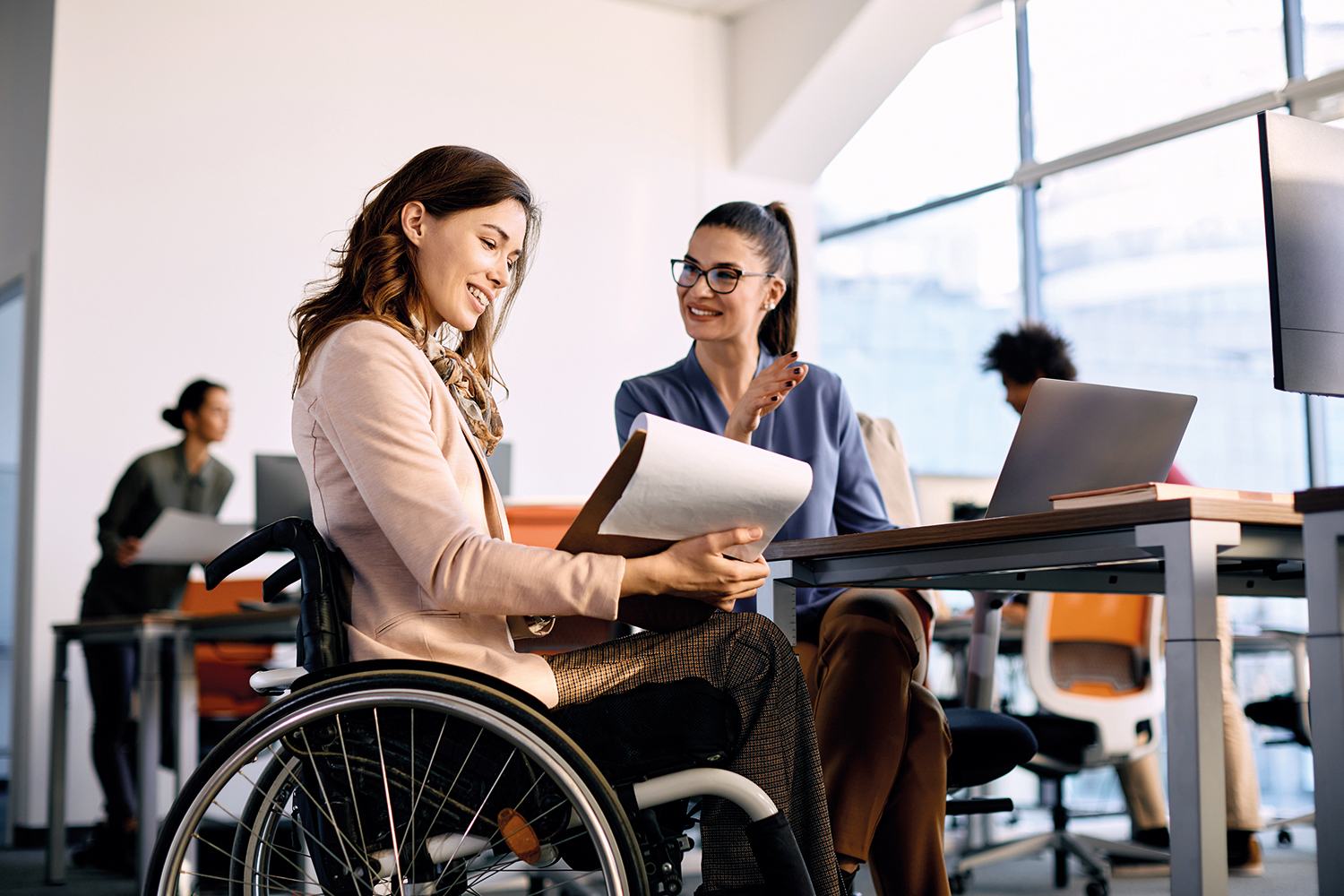 A woman in a wheelchair talking to a work colleague in the office